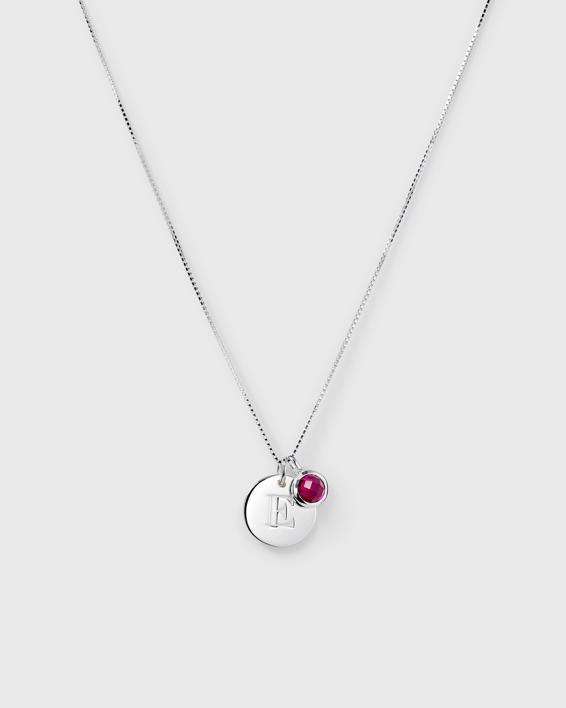 Silver chain with July birthstone ruby and round letter pendant.