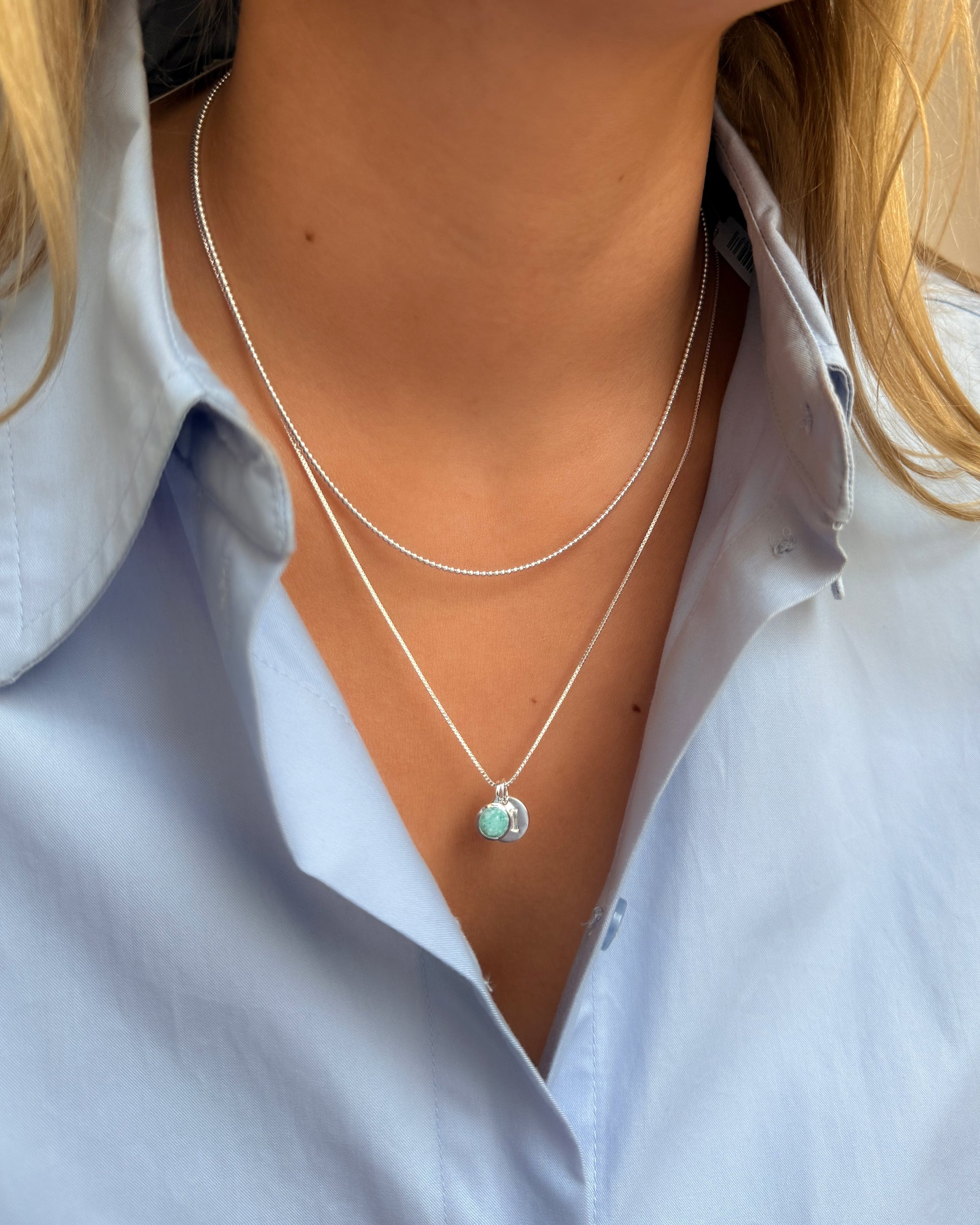 A silver pendant necklace featuring the December birthstone turquoise amazonite, layered with a shorter silver ball chain. 