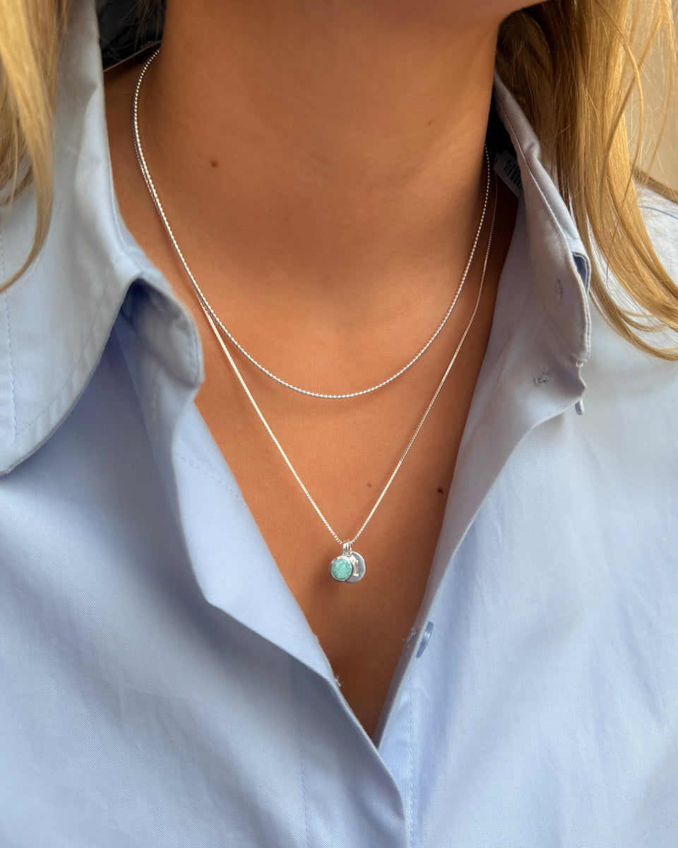 A silver pendant necklace featuring the December birthstone turquoise amazonite, layered with a shorter silver ball chain. 