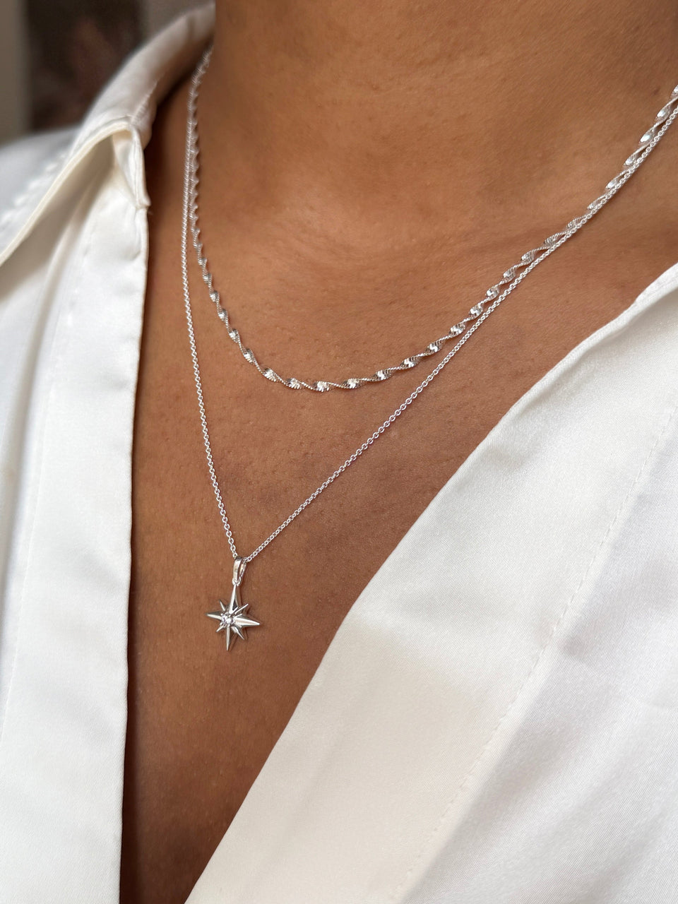A close-up of a model wearing the North Star & Herringbone Necklace Set in silver, showing the two necklaces layered against her skin.