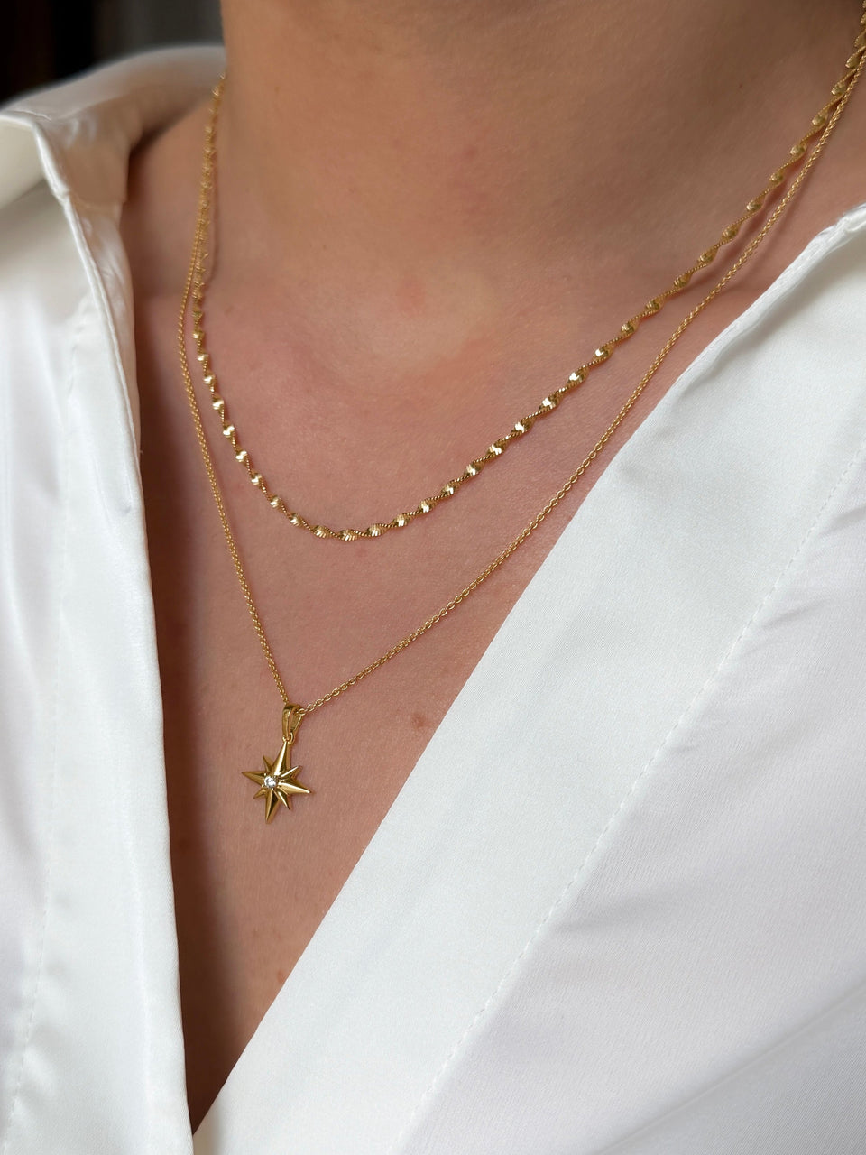 A close-up shot of a model wearing the layered North Star & Herringbone Necklace Set in gold, showcasing the shorter twisted chain and the longer chain with its crystal-embellished North Star pendant.