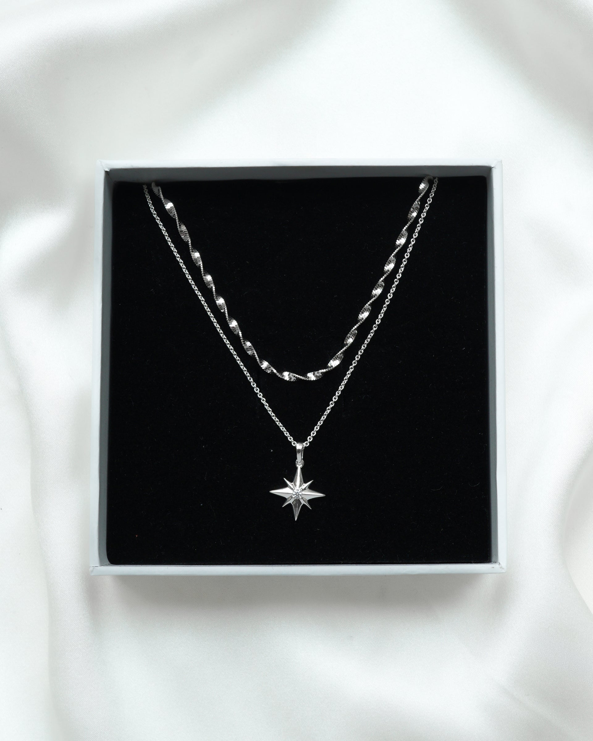 A product shot of the North Star & Herringbone Necklace Set in silver, displayed inside a white Syster P gift box, showing the twisted herringbone chain and the North Star pendant necklace.