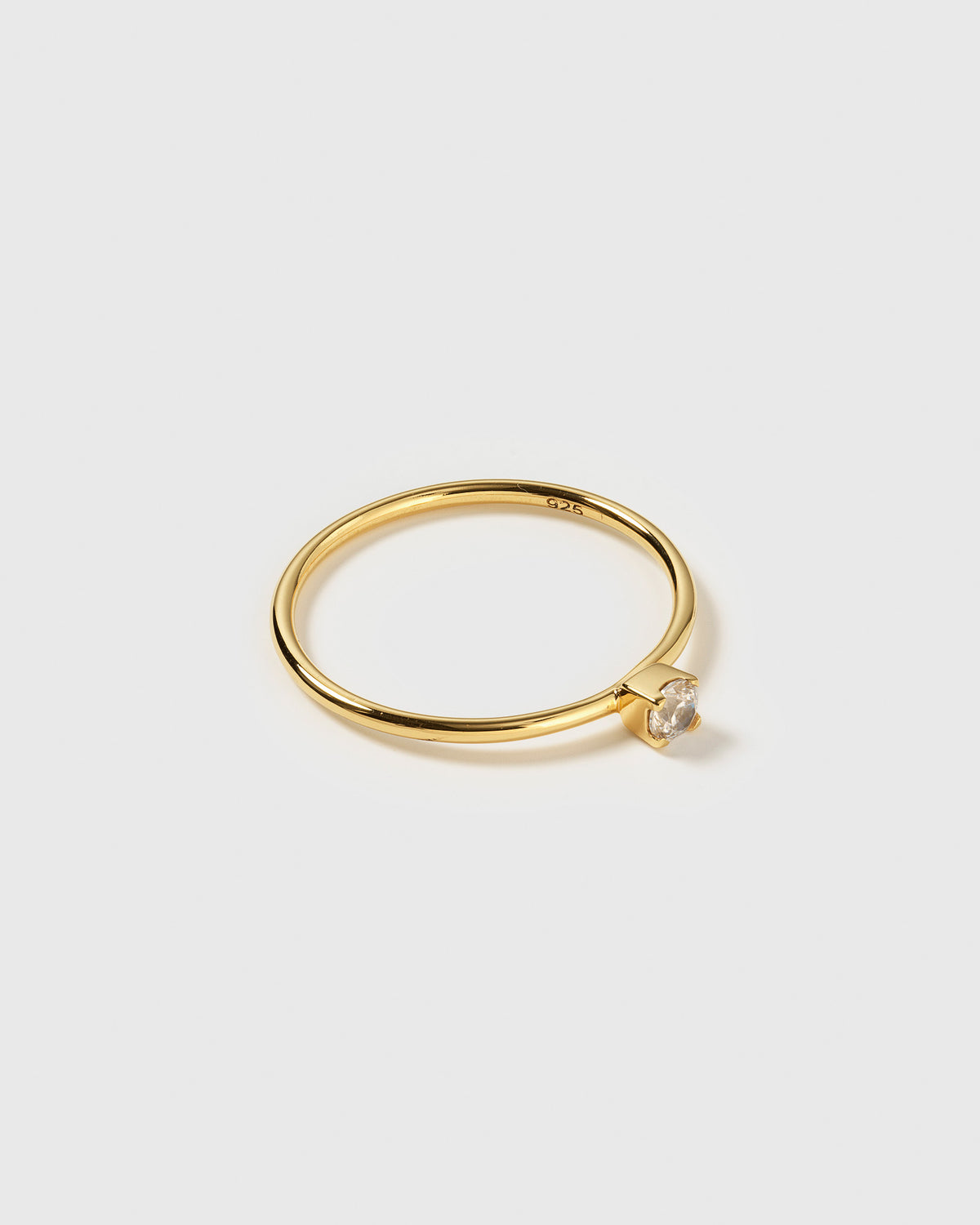 A product shot of the Tiny Princess Ring Gold, featuring a thin gold band and a single, round, faceted crystal in a princess setting.
