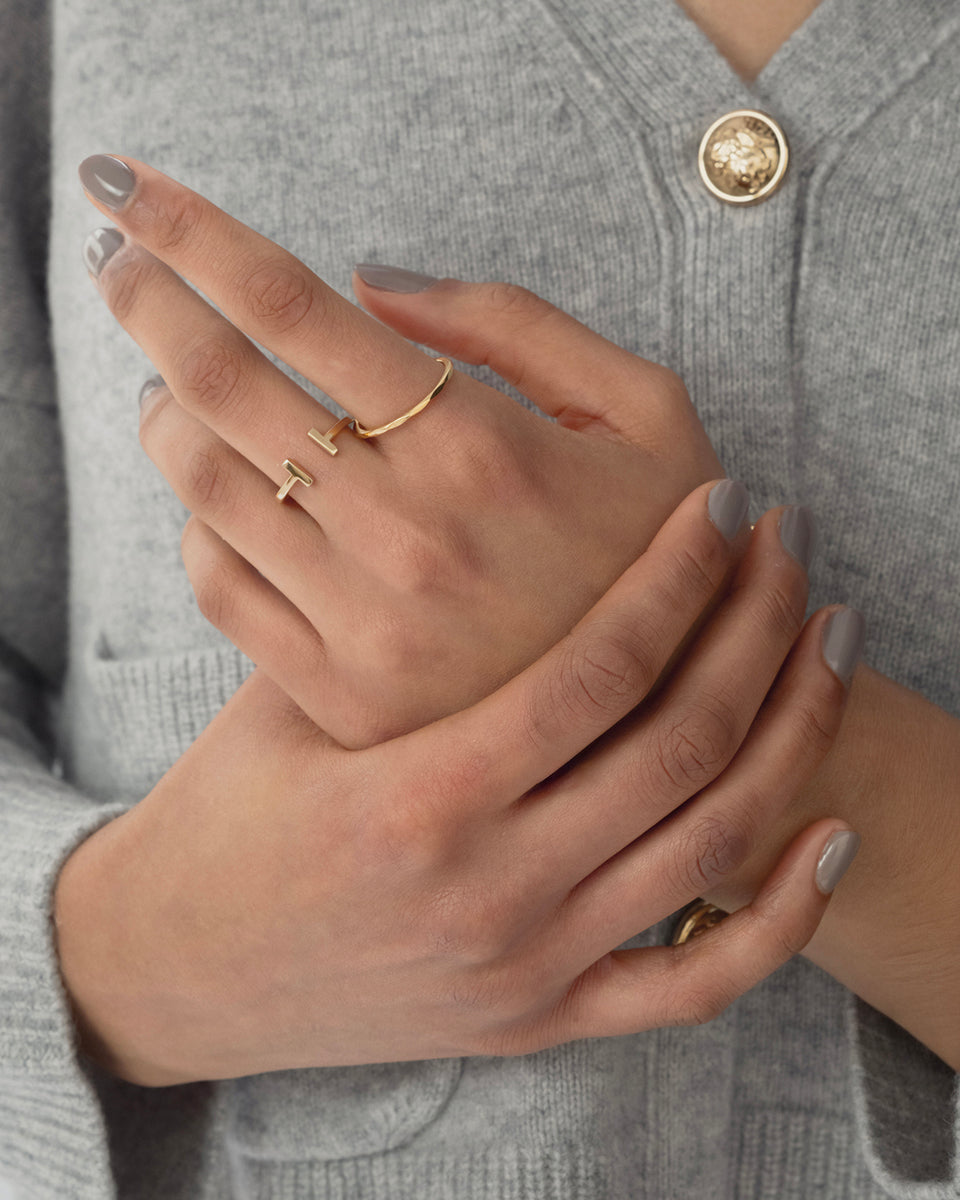 A model wearing the Strict Bar Ring in gold on her index finger, showcasing its open design with two parallel bars, and another simple gold band on her thumb.