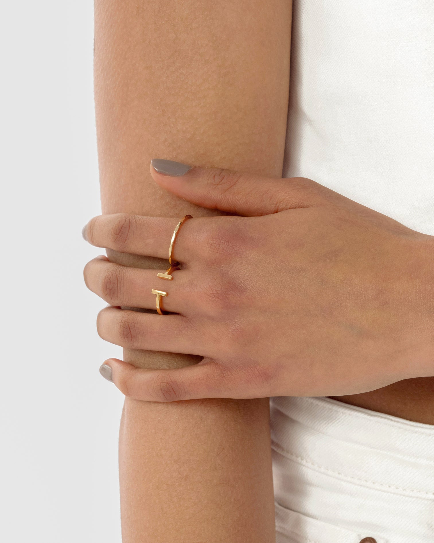 A model's hand wearing the Strict Bar Ring in gold, showcasing its open design with two bar-shaped ends.