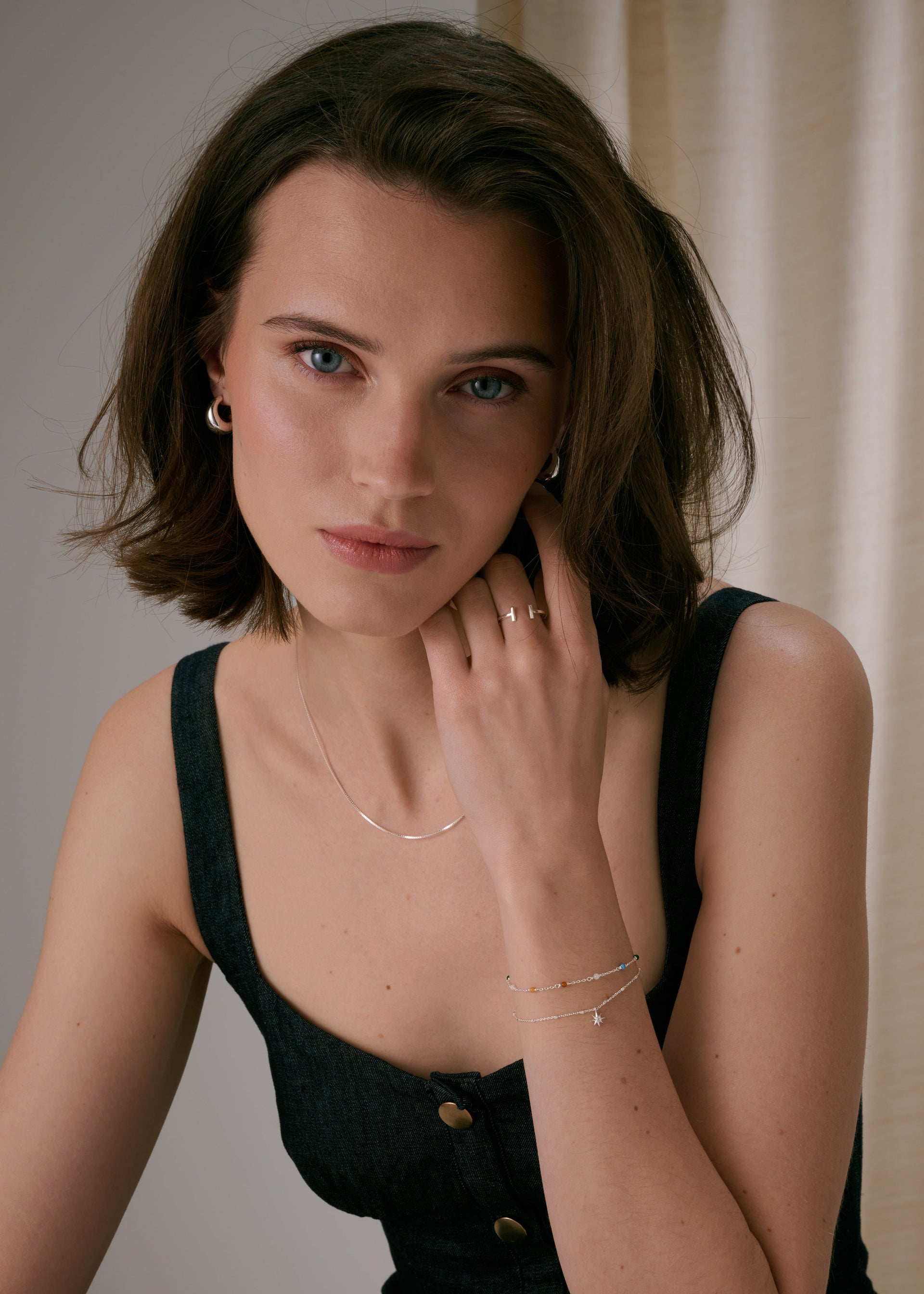 A ring in silver, along with small silver hoop earrings, a thin silver chain necklace, and two delicate chain bracelets.