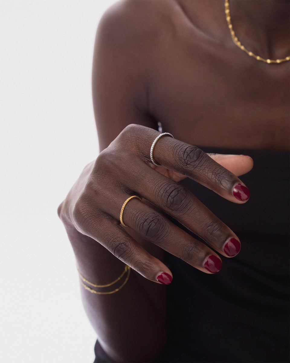 A close-up of a model wearing the Tiny Sparkle Ring in gold on her ring finger and the silver version on her index finger, accessorized with a delicate gold necklace and bracelet.
