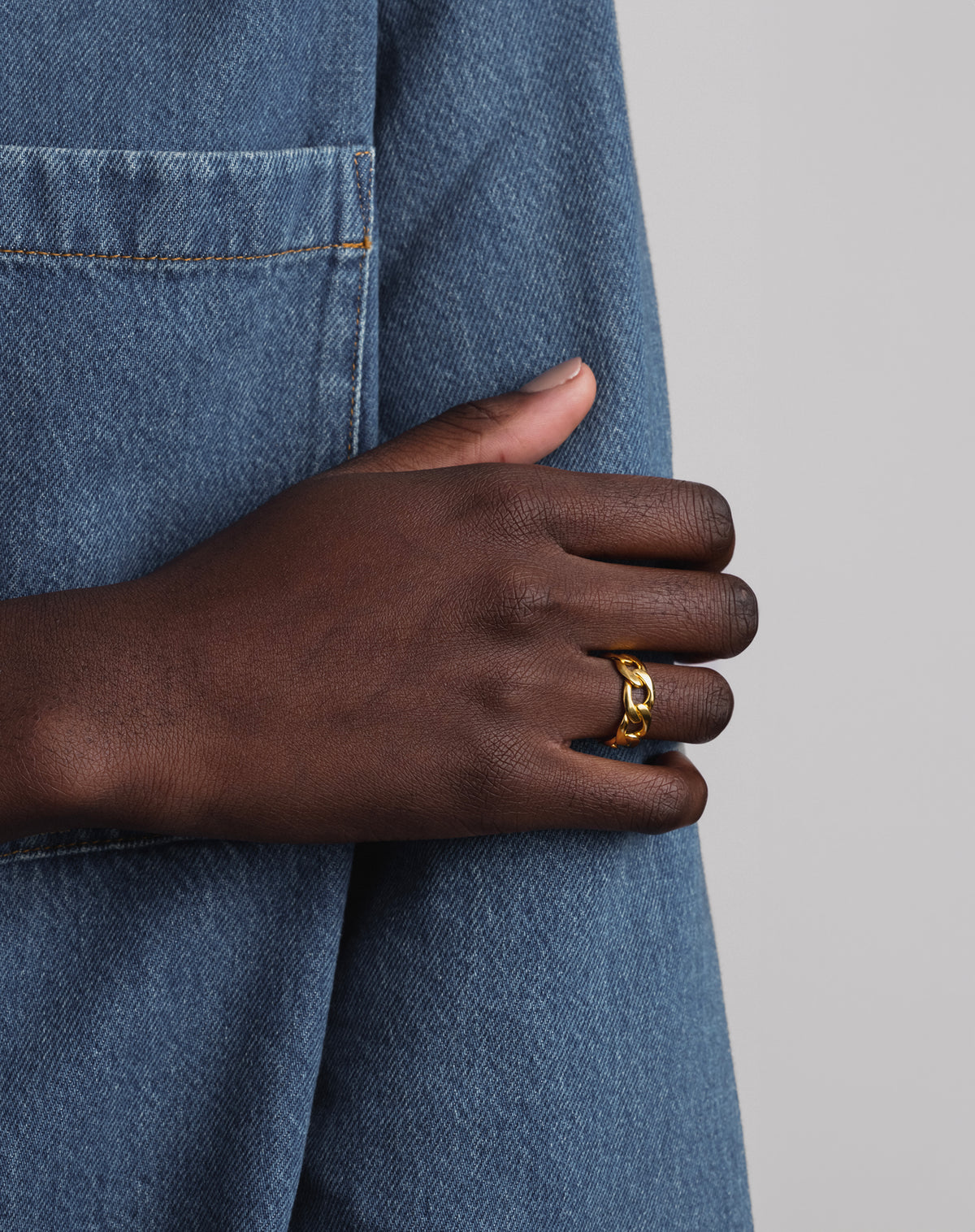 A model's hand resting on the sleeve of a denim jacket, showcasing the bold Links Ring in gold with its curb chain design.
