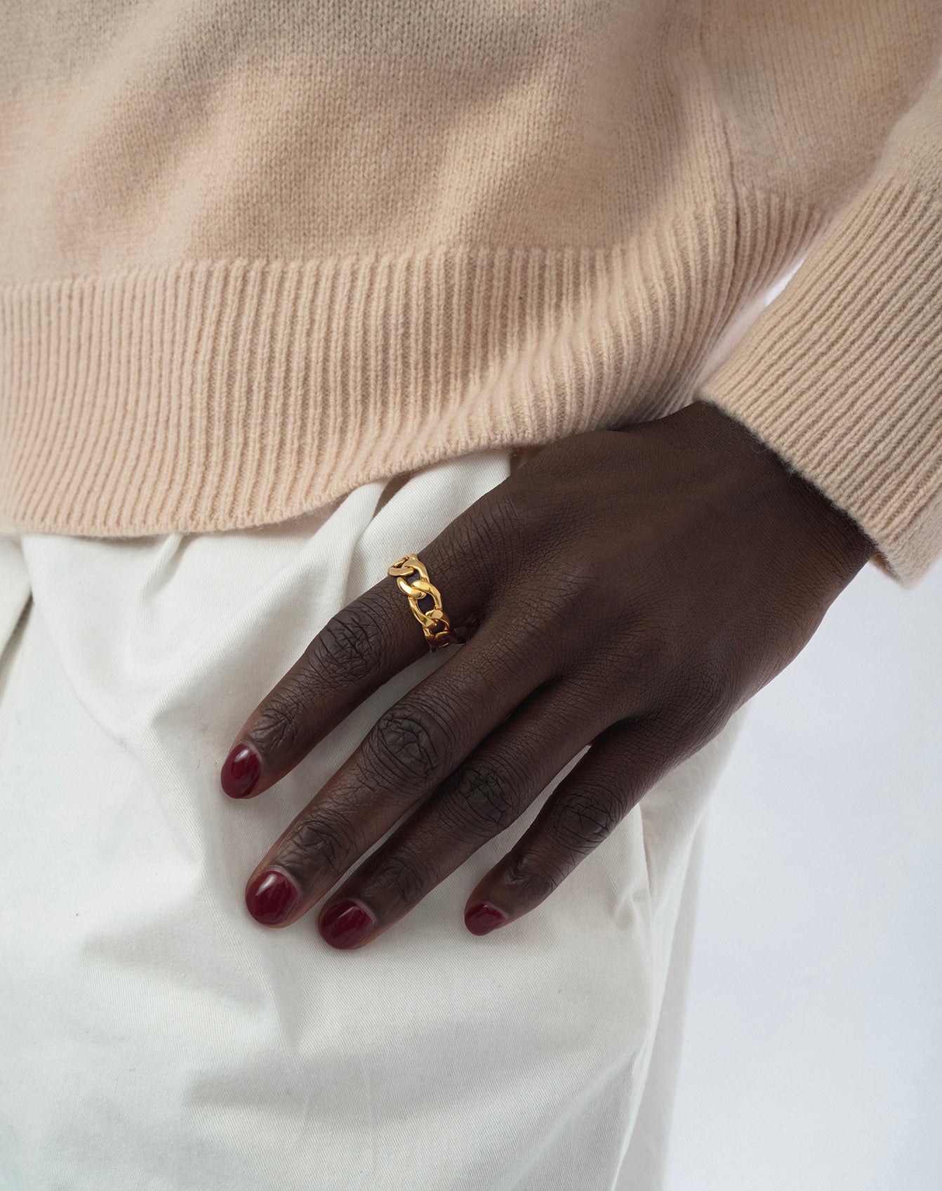 A model wears the Links Ring Gold, showcasing its curb chain design on her finger, styled with a beige knit sweater and white trousers.