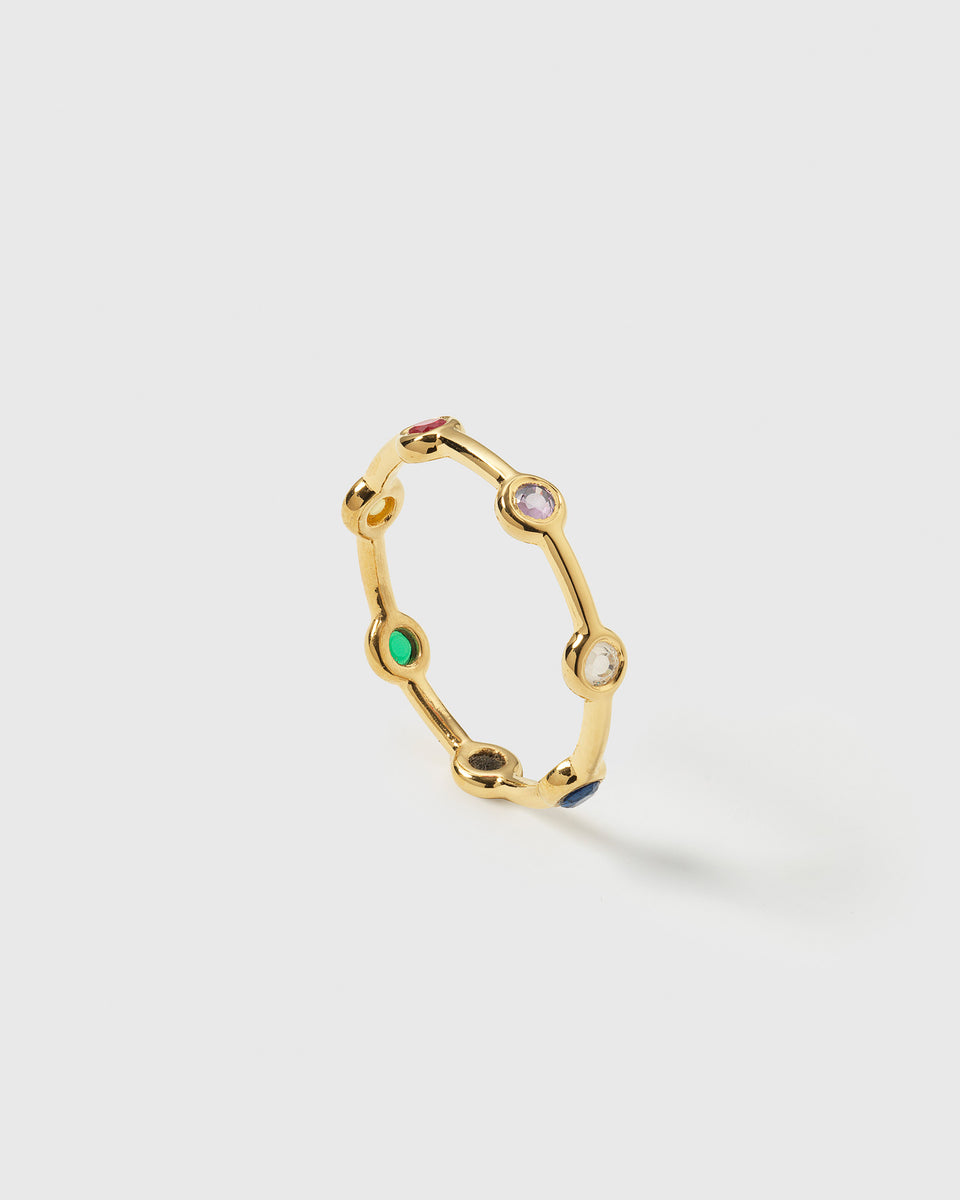 A product shot of the Treasure Shimmer Ring in gold, showing its design of a delicate band adorned with bezel-set, multi-colored zirconia stones.