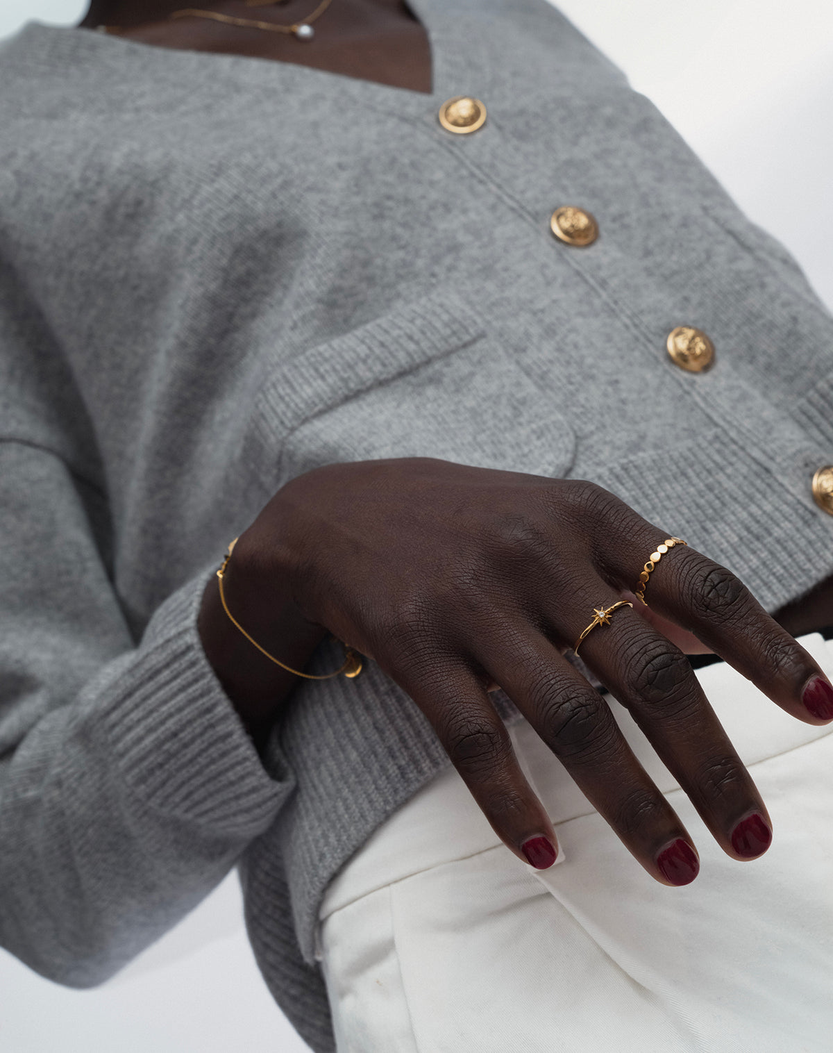 A model styles the gold North Star Ring, which features a delicate star with a central crystal, with a second gold ring that has a dotted design. A fine gold chain bracelet and a delicate pearl necklace complete the elegant look.