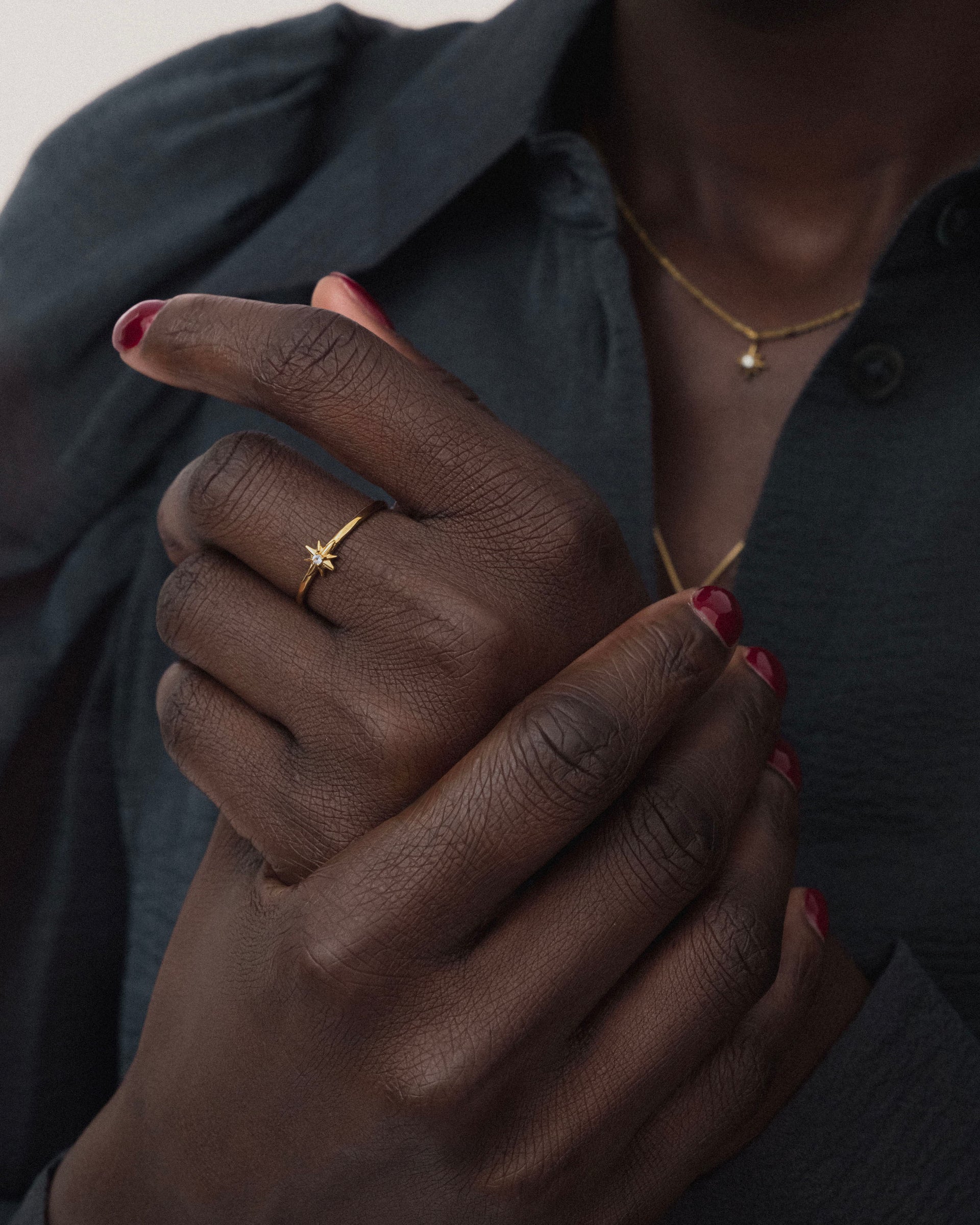 A close-up shot of a model wearing the North Star Ring in gold, featuring a star design with a central crystal, along with a matching necklace.