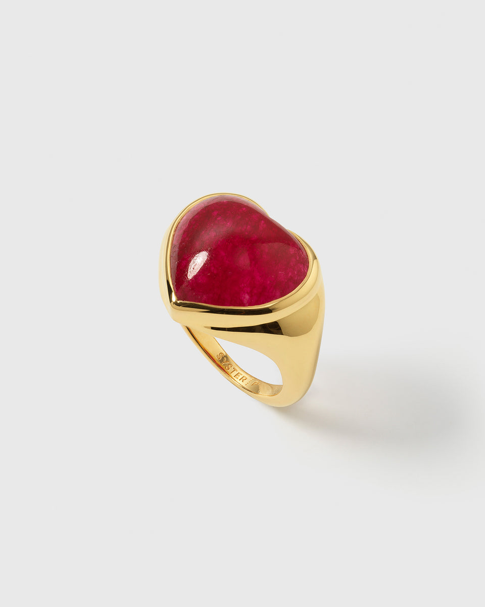 A product shot of the La La Love Big Heart Ring in gold, featuring a large, vibrant pink quartz stone cut into a heart shape and set on a chunky gold band.