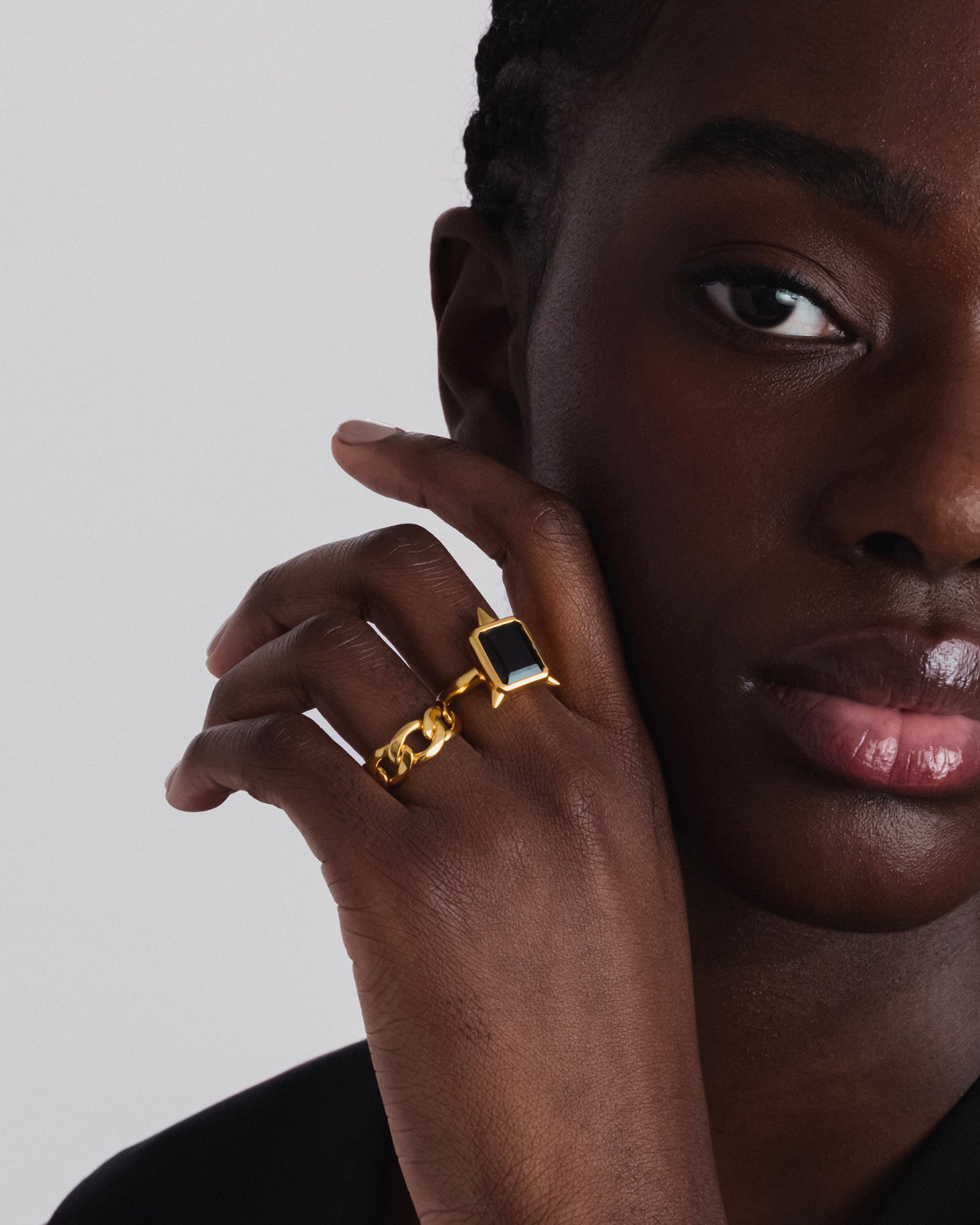 A close-up of a model wearing the Drama Ring Gold, featuring a large, rectangular smokey quartz gemstone with spike details, and the Bold Chain Ring Gold.