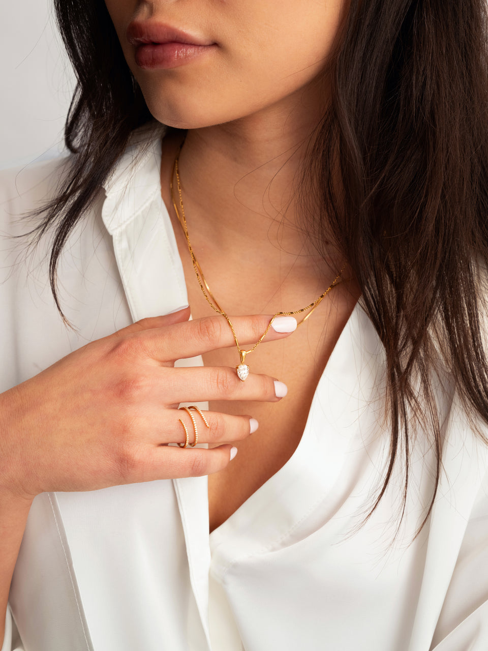A model wearing the gold Sparkle Wrap Ring, which elegantly coils around her finger studded with tiny crystals, paired with a simple gold chain necklace featuring a pear-shaped crystal pendant.