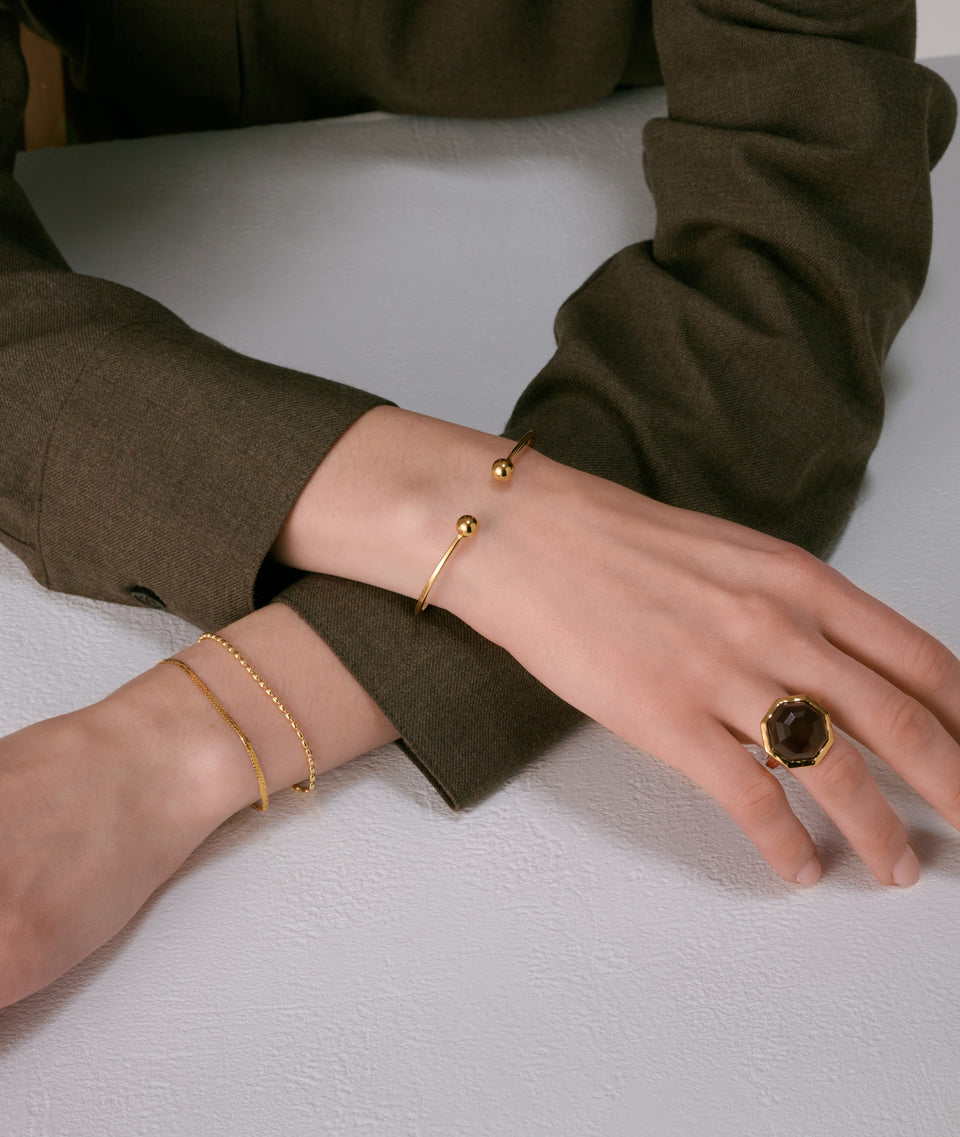 A statement ring with an octagon-shaped faceted smokey quartz and gold plated bracelets.