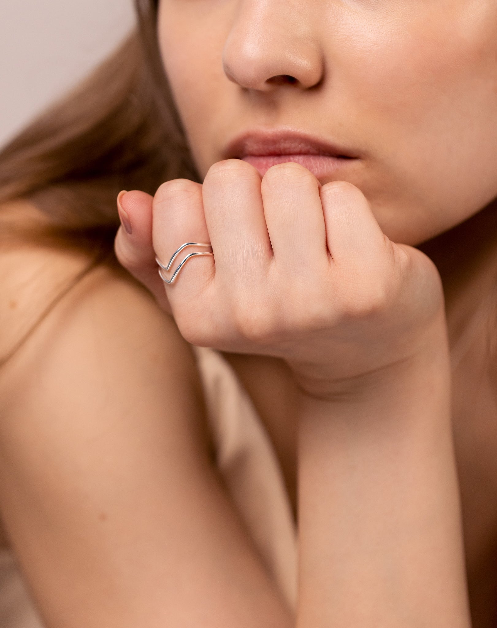 A close-up shot of a model wearing the Tiny Arrow Ring in silver, showcasing its delicate double arrow design on her finger.
