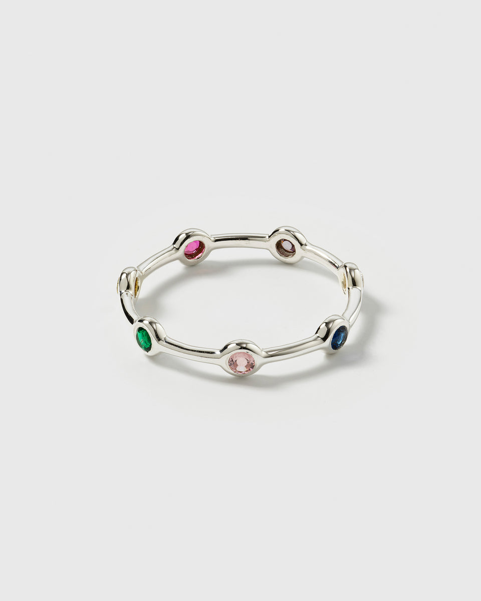 A product shot of the Treasure Shimmer Ring in silver, showcasing its delicate band design set with various colorful, faceted zirconias.