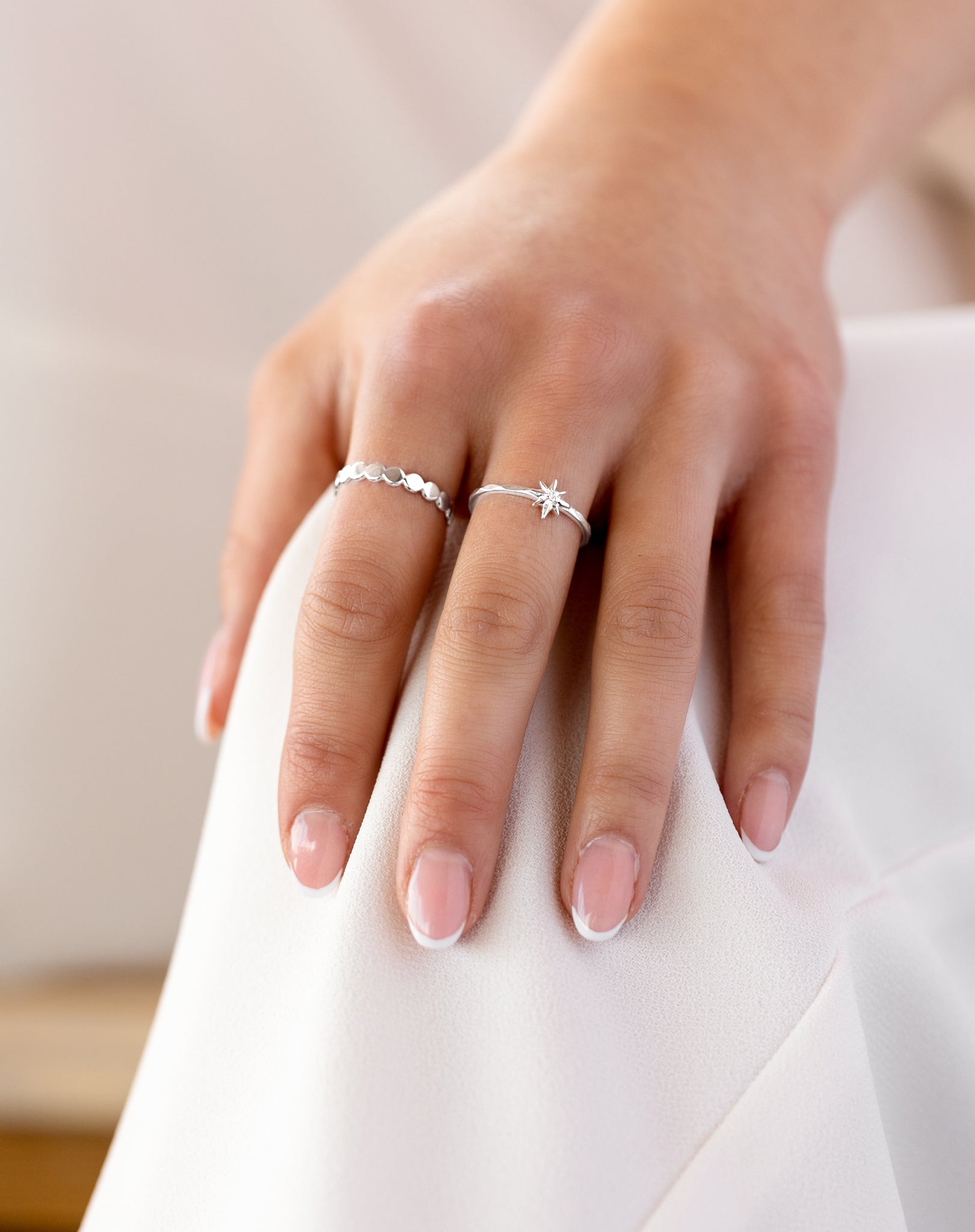 A close-up shot of a model's hand wearing the North Star Ring in silver on the middle finger, featuring a small star with a crystal, alongside another silver ring with a pattern of flat circles on the index finger.