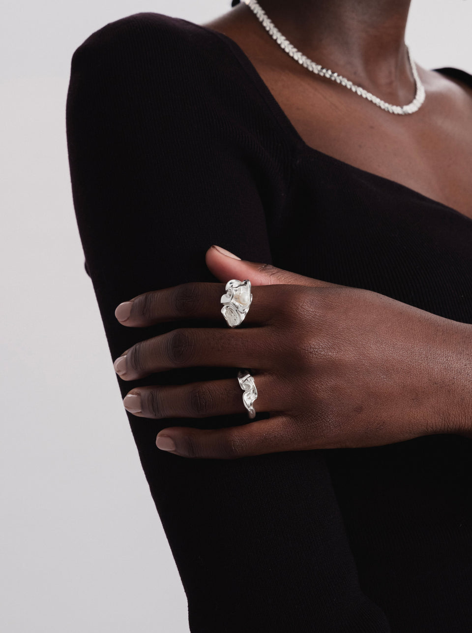 A model wearing the organically shaped Moulded Big Ring Silver with a freshwater pearl on her index finger, paired with a smaller moulded silver ring on another finger and a textured silver necklace.