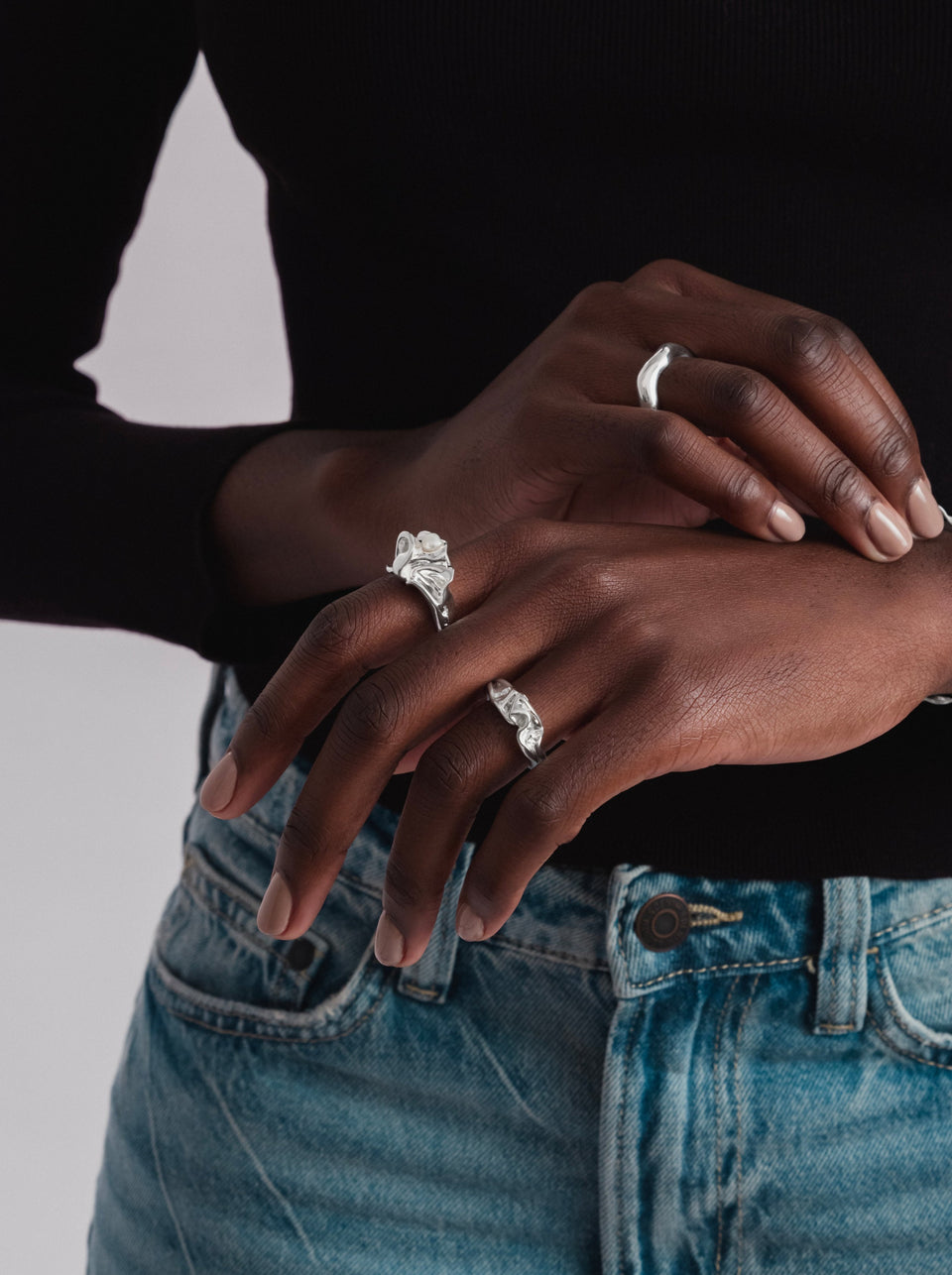 A model with her hands crossed, wearing the Moulded Narrow Ring Silver on her left index finger, styled with a wider smooth silver ring and another detailed moulded silver ring.