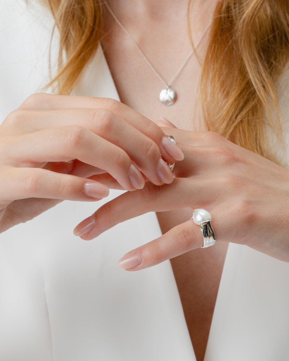 A model wearing the Paxton Ring, a hammered silver ring with a large baroque pearl. She is also wearing a silver pendant necklace.