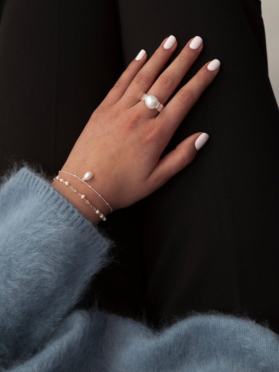 Model wearing the silver Paxton Ring with a large pearl on her finger and two delicate silver pearl bracelets around her wrist.