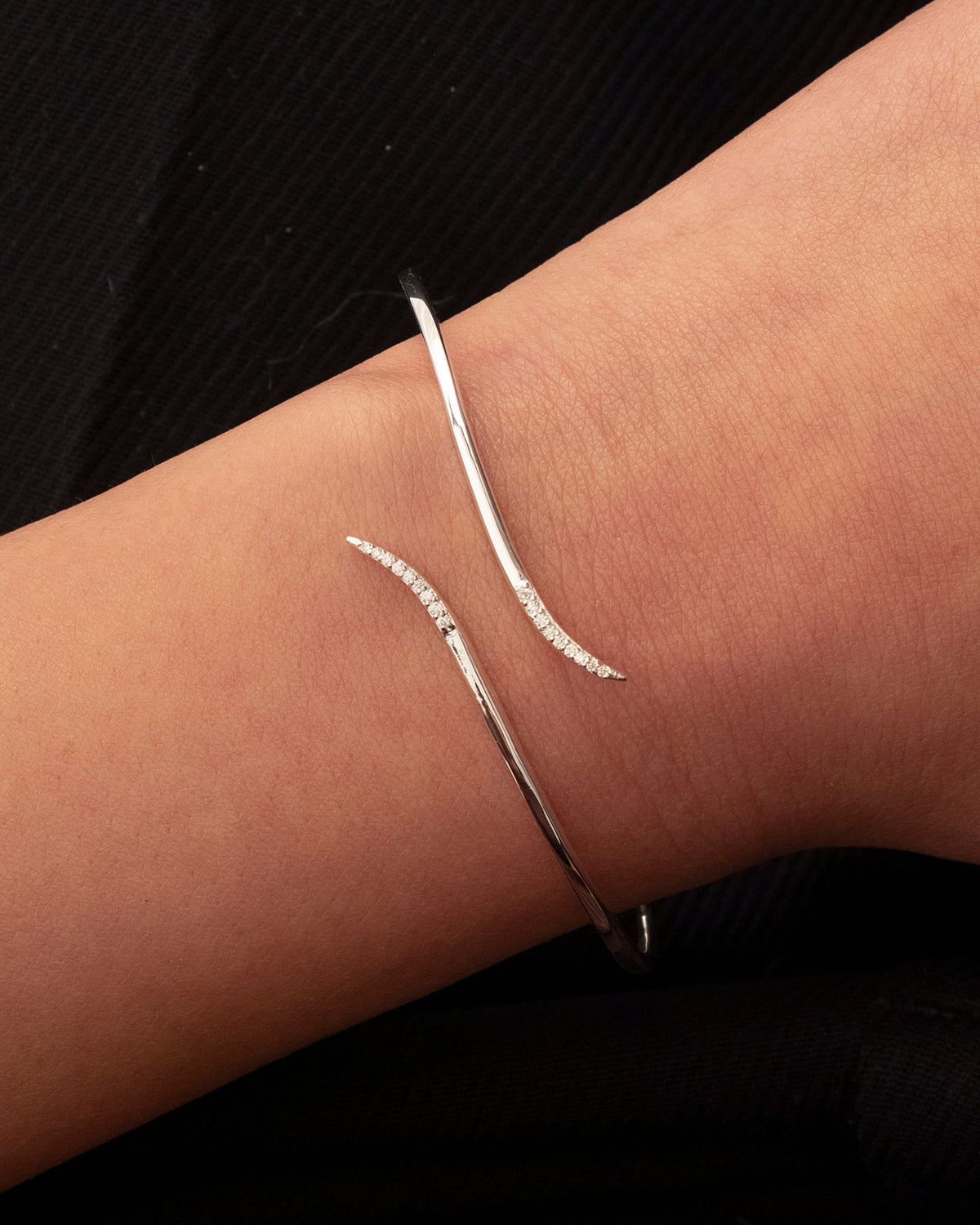 A close-up of a model wearing the Sparkle Wrap Bangle in silver, showcasing its delicate wrap design with curved ends adorned with cubic zirconia stones.