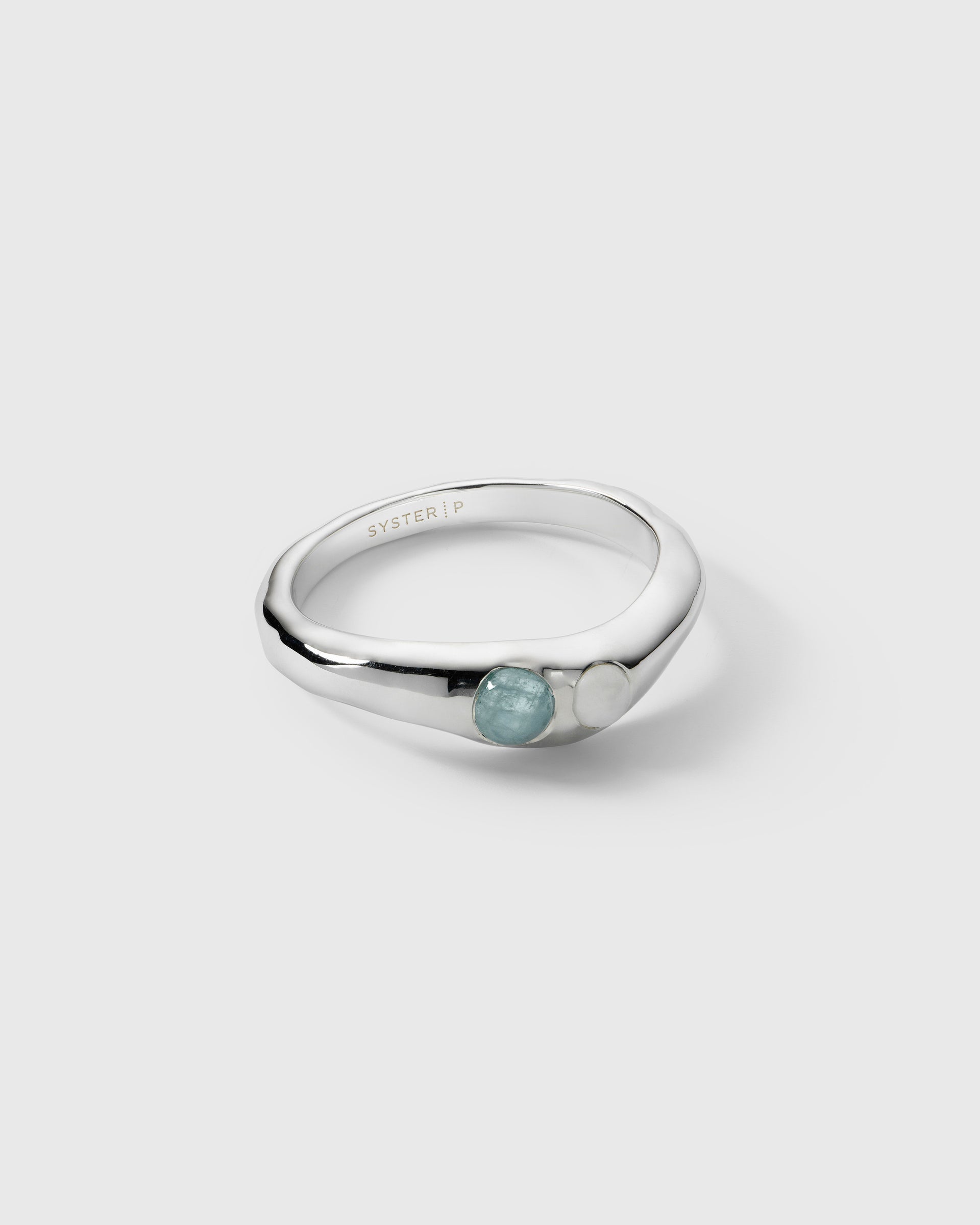 A product shot of the Florentina Ring in silver, showcasing its wavy band set with a light blue aquamarine and a white moonstone.