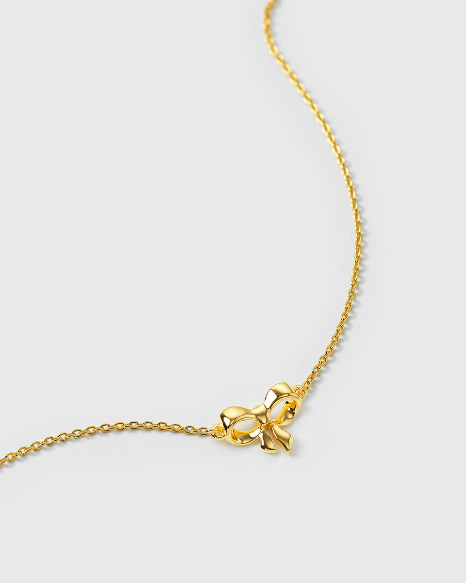 A close-up product shot of the Rosie Mini Bracelet Gold, focusing on the small, polished bow pendant attached to its structured, sparkling chain.