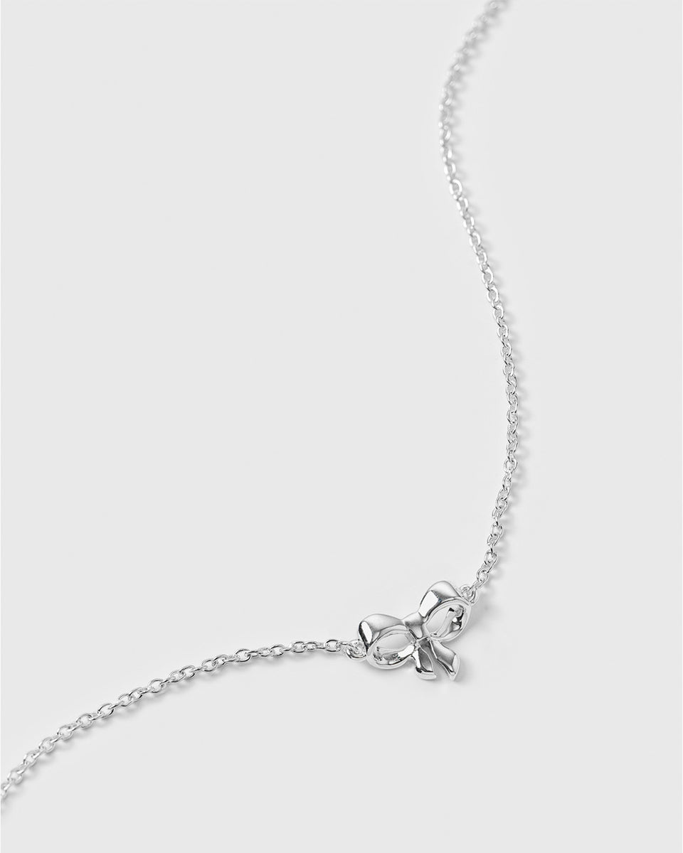 A close-up shot of the Rosie Mini Bracelet in silver, showing its delicate chain and a small, detailed bow pendant.