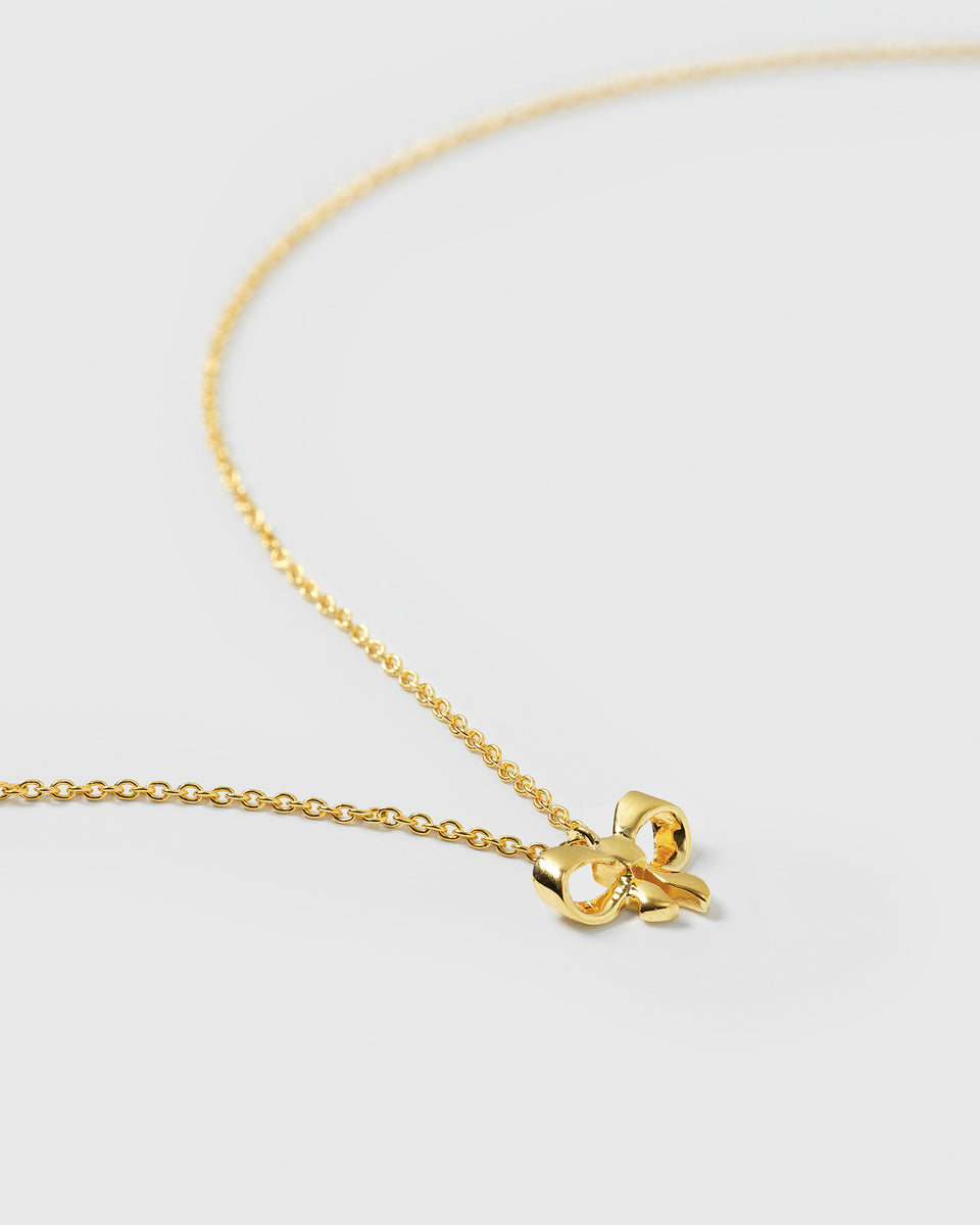 A product shot of the Rosie Mini Necklace in gold, laid out in a gentle curve to display its small bow pendant and sparkling, structured chain.