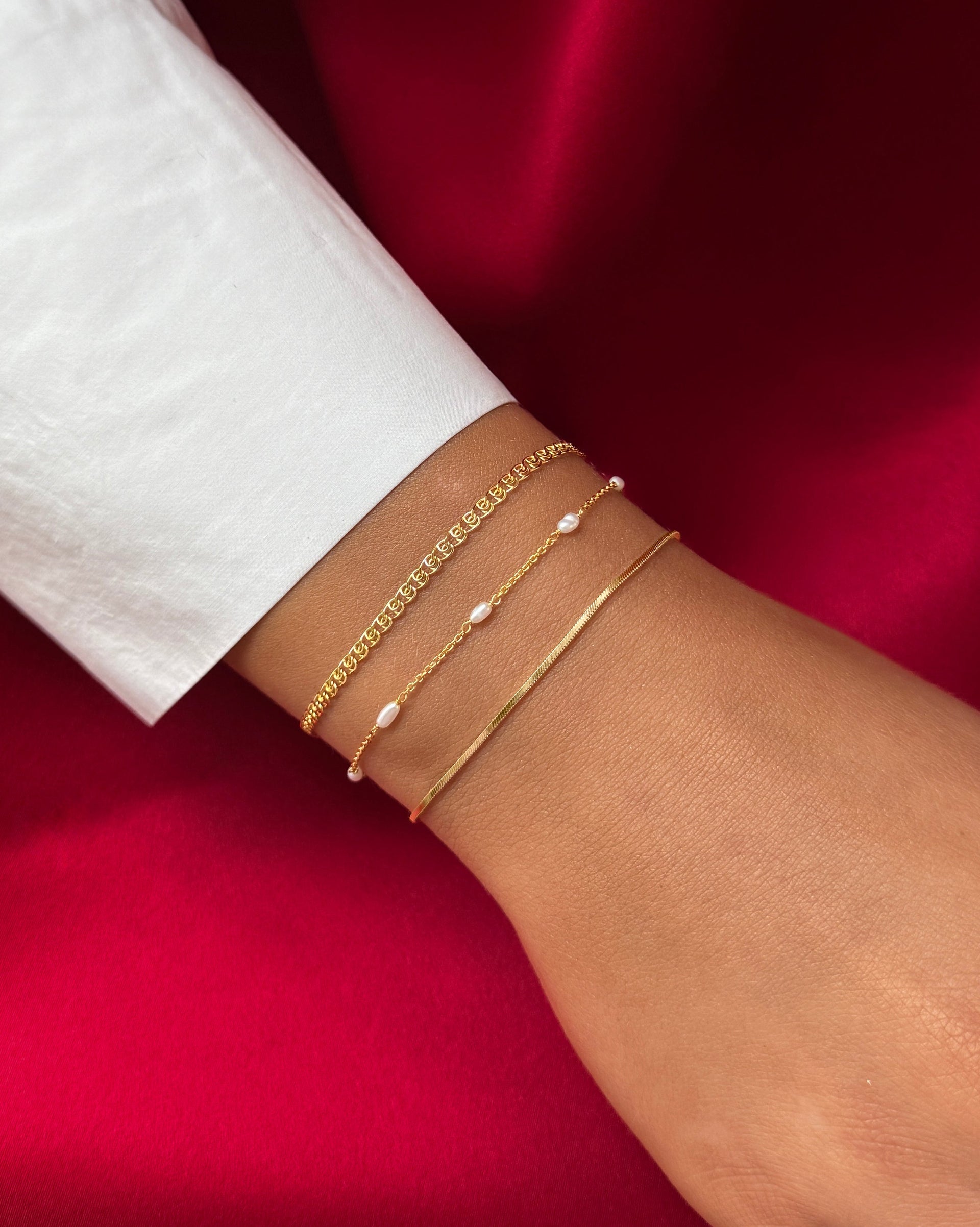 A close-up of the gold Sheer Love Bracelet with its unique patterned chain, shown stacked on a model's wrist with the Treasure Multi Pearl Bracelet and the Sheer Mirror Bracelet.
