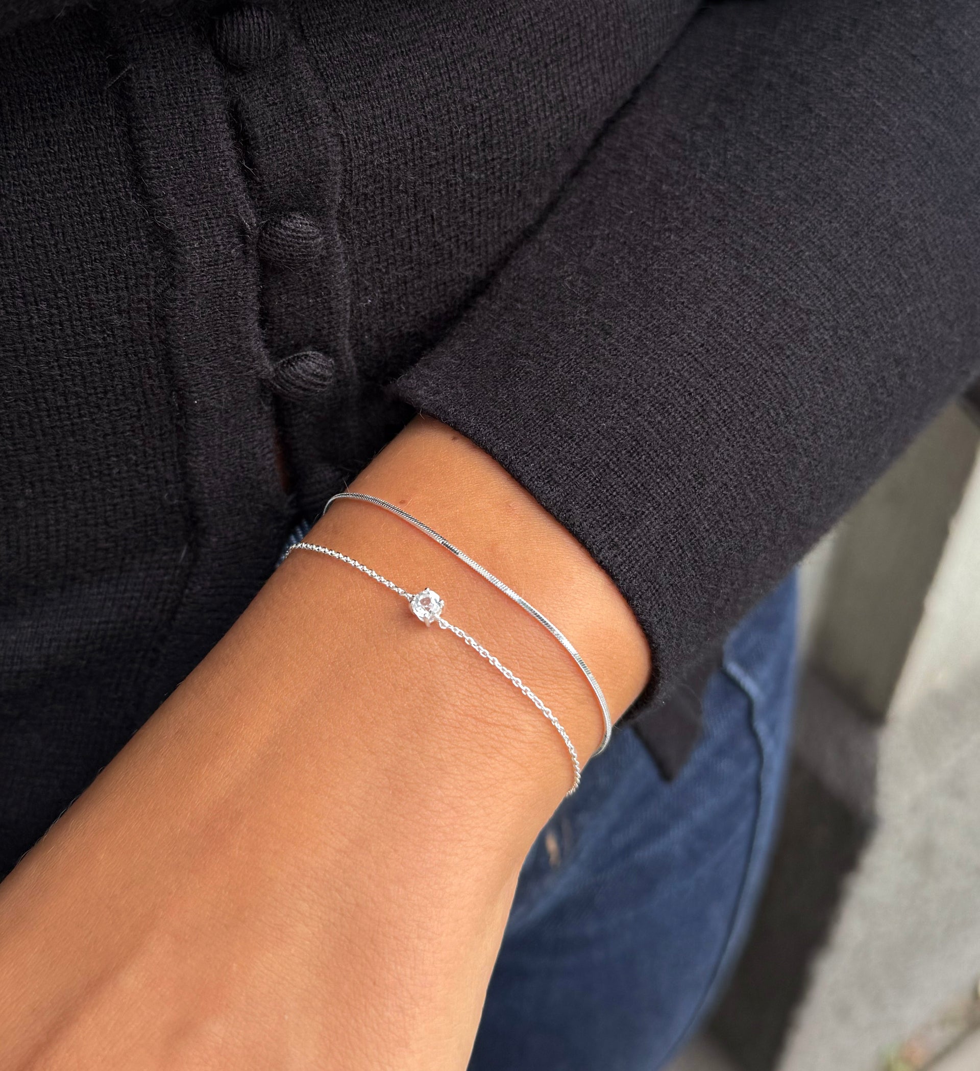 A model wearing the Minimalistica Solo Nova Bracelet in silver, a delicate chain with a single white topaz, layered with the sleek Sheer Mirror Bracelet, also in silver.