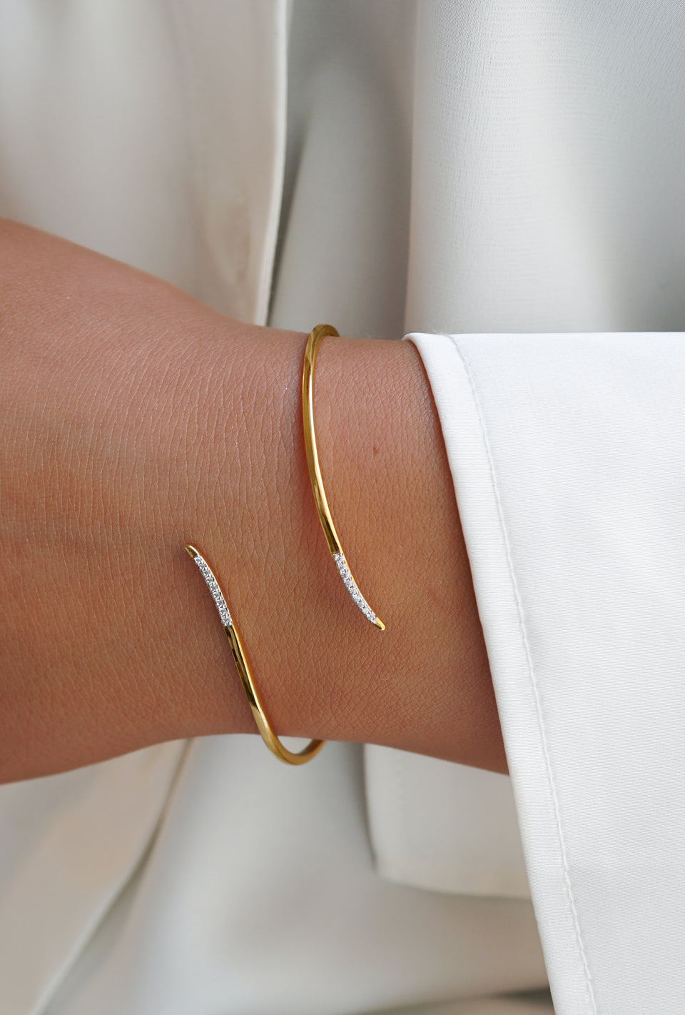 A close-up of a model wearing the Sparkle Wrap Bangle in gold, showcasing its elegant wrap design with ends adorned with sparkling cubic zirconia.