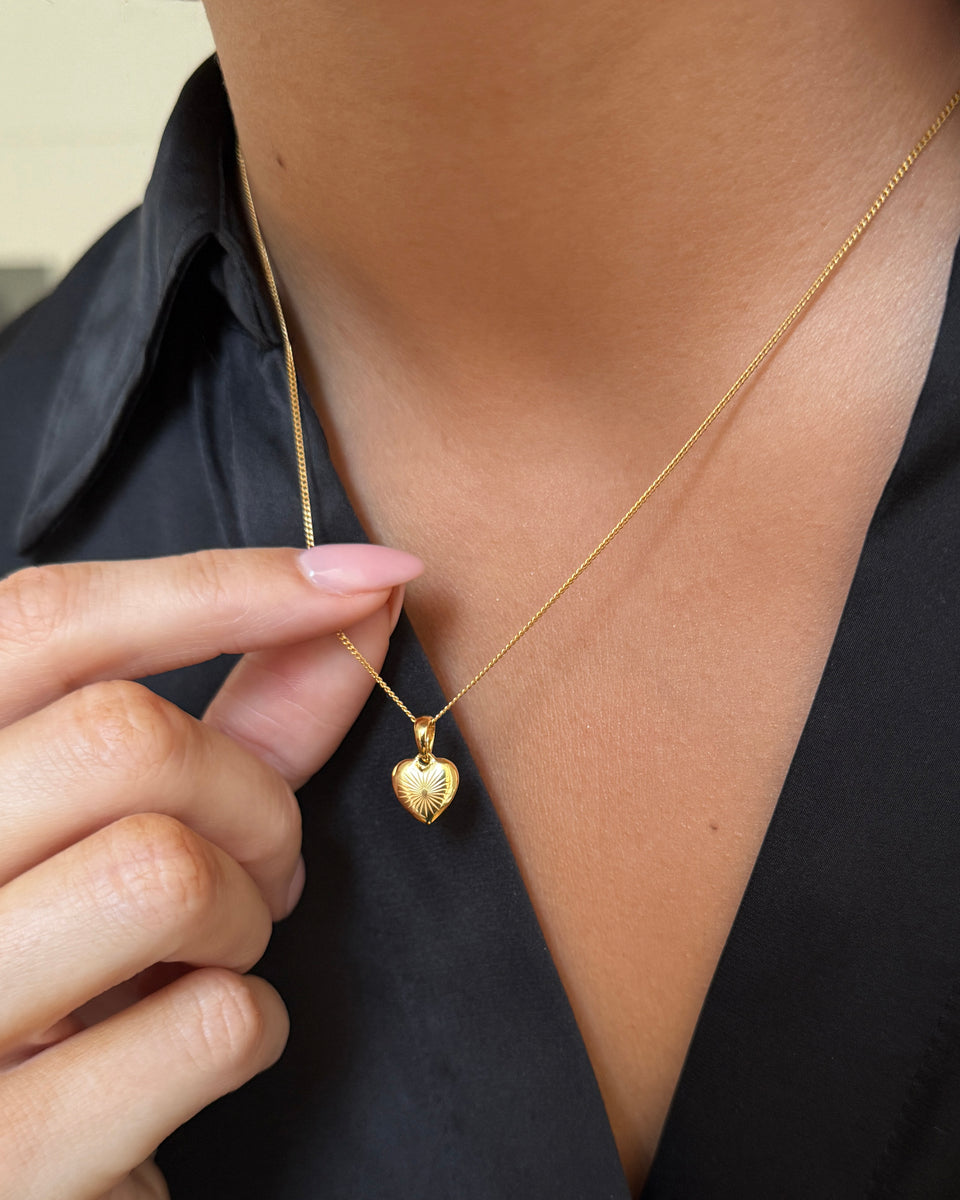 A close-up shot of a model wearing the Sunburst Heart Necklace in gold, showcasing the detailed sunburst pattern on the heart-shaped pendant.
