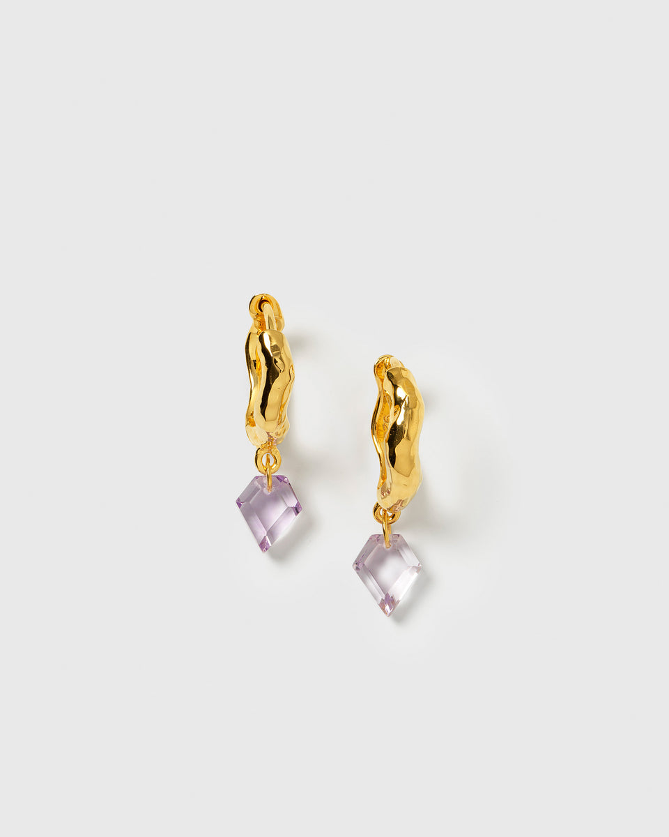 A product shot of the Diamona Earrings in gold, featuring a wavy, hammered hoop with a dangling, diamond-shaped amethyst stone.