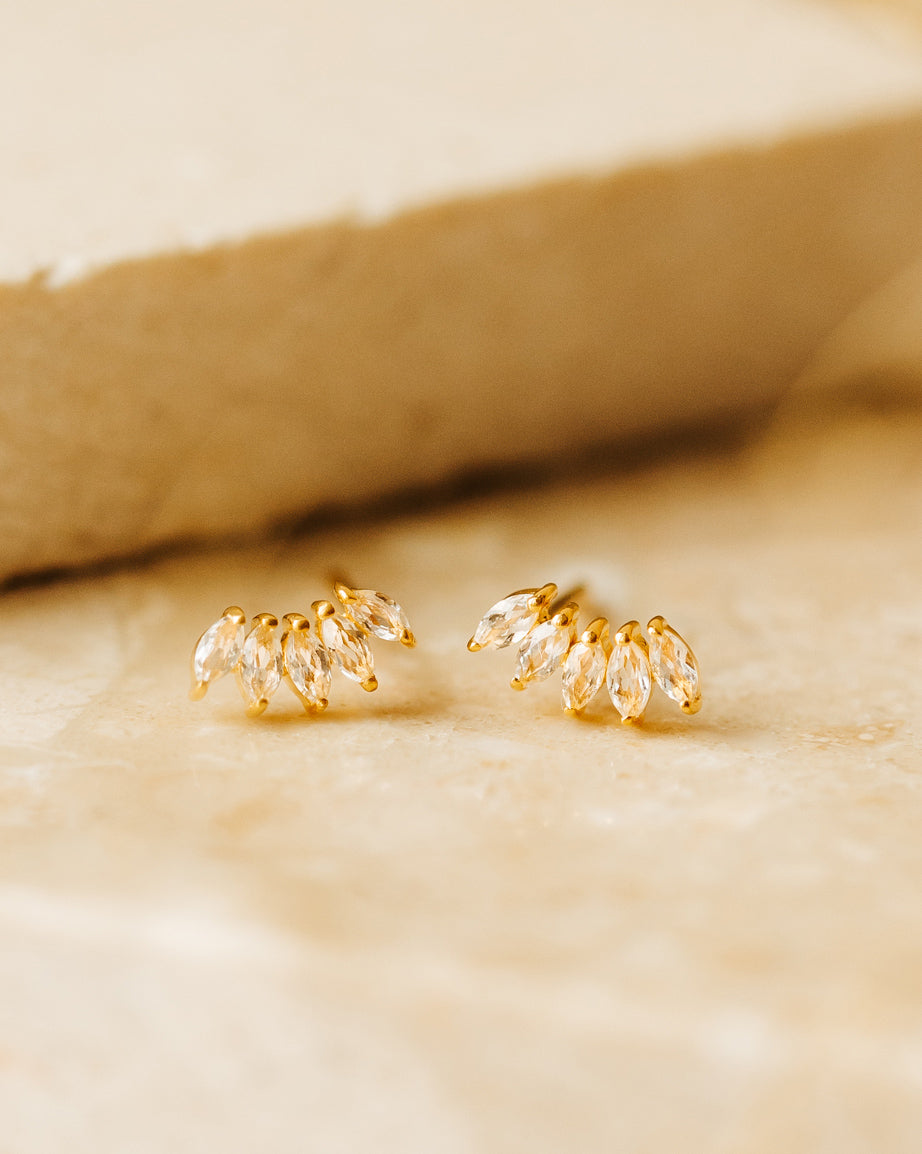 A product shot of the Theodora Earrings in gold, a pair of studs each adorned with four fanned-out, marquise-cut cubic zirconia stones.