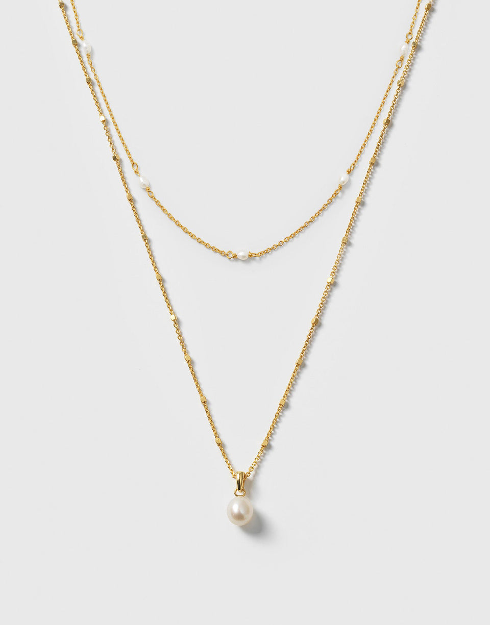 A product shot of the Treasure Necklace Set Gold, featuring two layered necklaces: a shorter one with multiple small freshwater pearls and a longer one with a single pearl pendant.