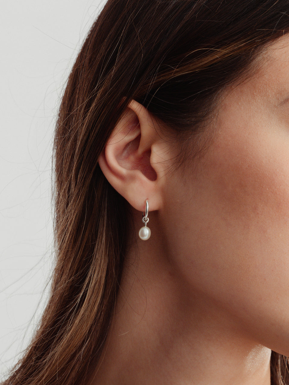 A close-up shot of a model wearing the Treasure Pearl Hoops in silver, featuring a delicate hoop with a dangling freshwater pearl.