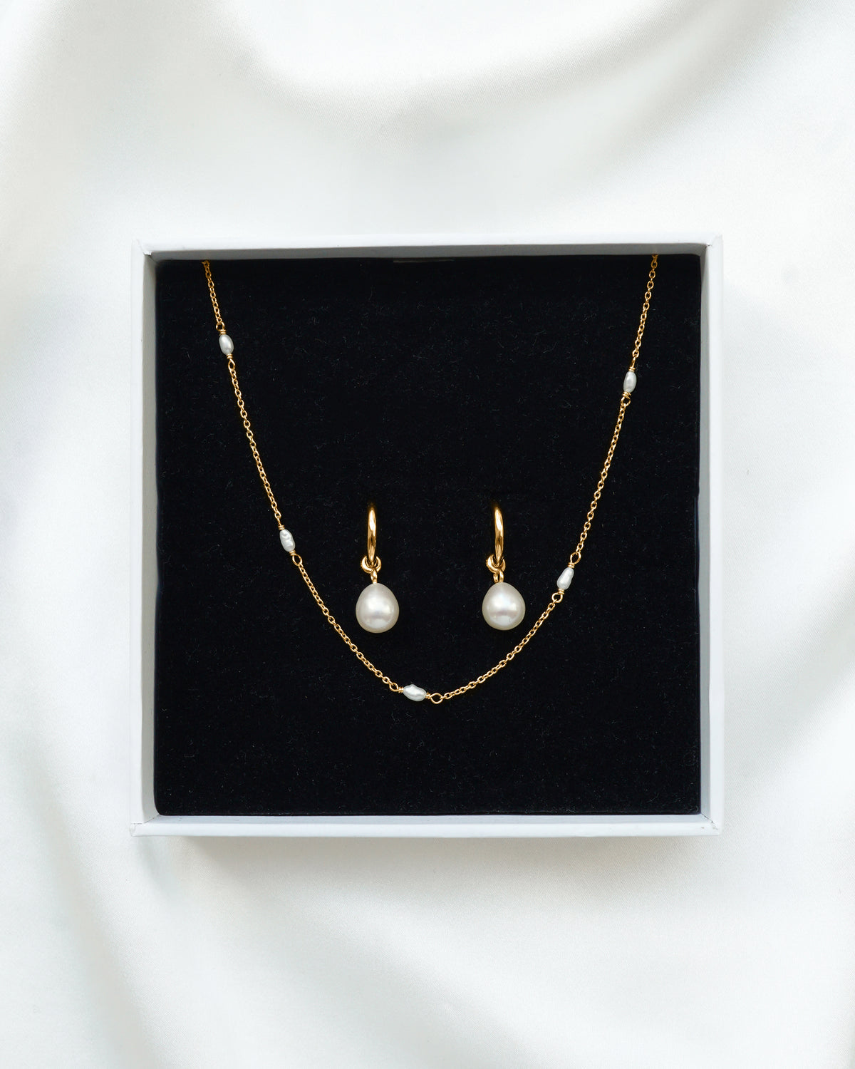A product shot of the Treasure Necklace & Earrings Set in gold, displayed in its Syster P gift box. The set includes a delicate gold chain necklace with small freshwater pearls and a pair of matching hoop earrings with larger dangling pearl charms.