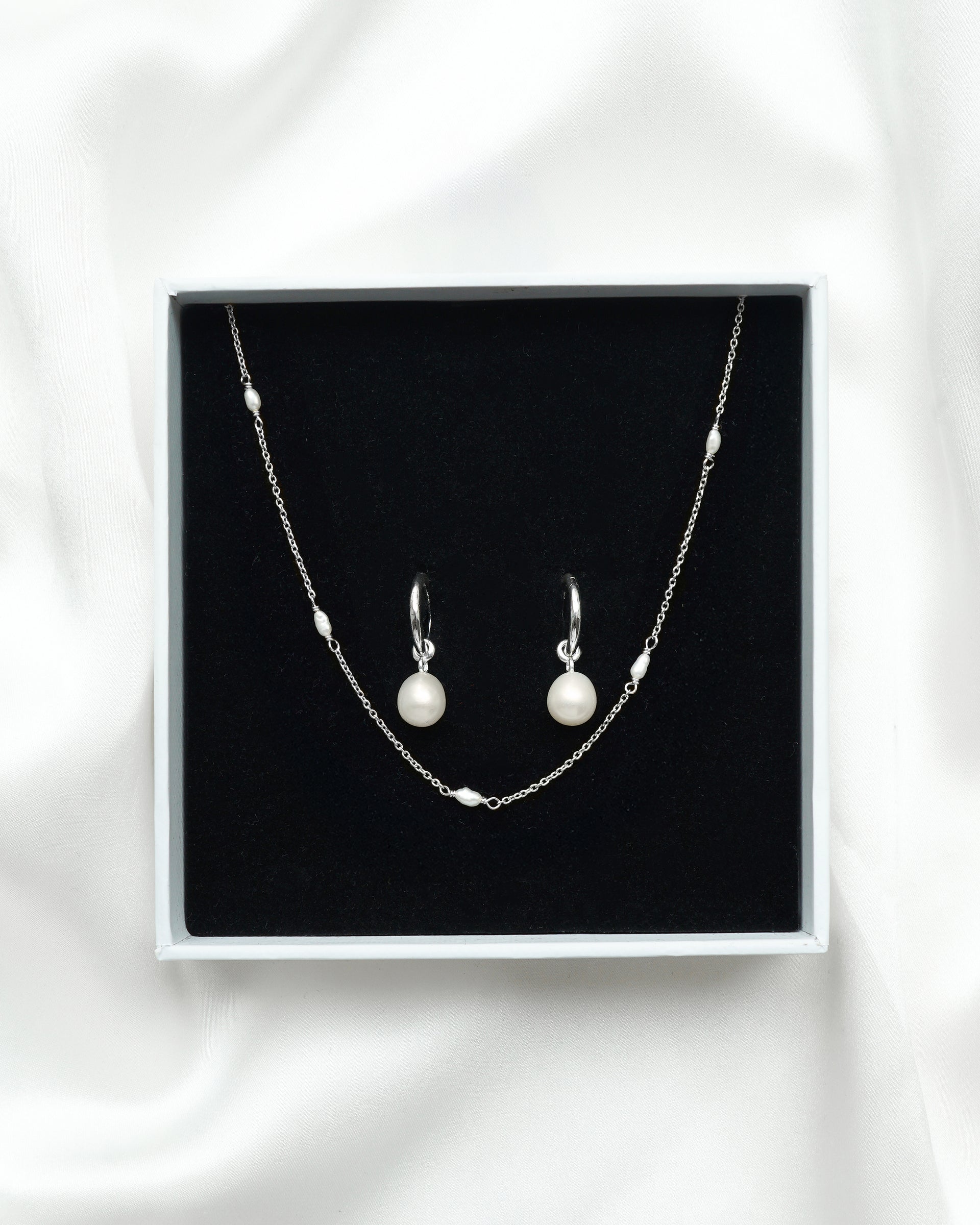 The Treasure Necklace & Earrings Set in silver, displayed in a white Syster P gift box, showcasing the fine chain necklace interspersed with small freshwater pearls and the matching hoop earrings with dangling round pearls.