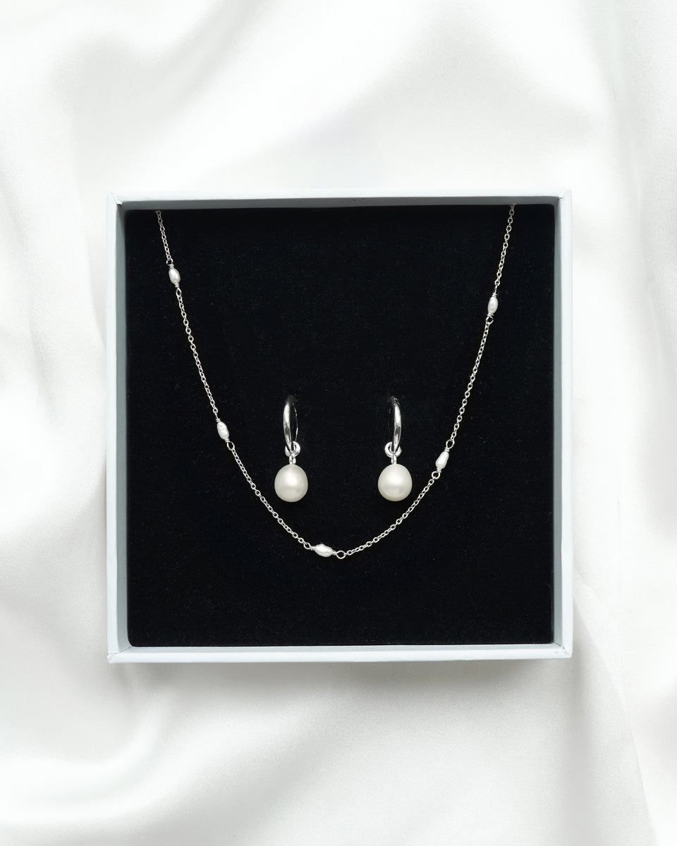 The Treasure Necklace & Earrings Set in silver, displayed in a white Syster P gift box, showcasing the fine chain necklace interspersed with small freshwater pearls and the matching hoop earrings with dangling round pearls.
