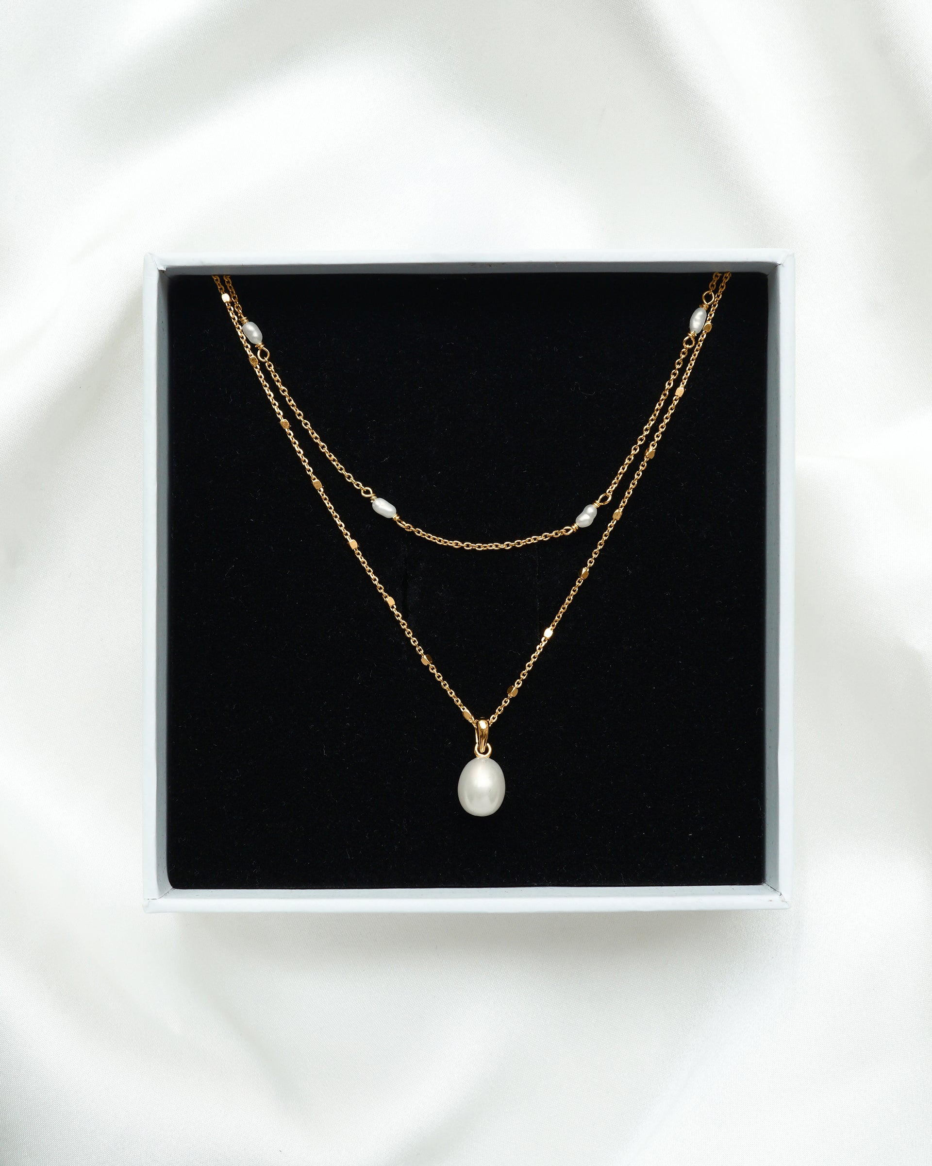 The Treasure Necklace Set in gold, featuring two layered freshwater pearl necklaces, presented inside a white Syster P gift box.