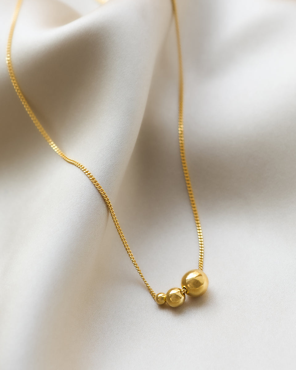 A product shot of the Universe Necklace Gold, highlighting its delicate gold chain adorned with three balls in graduating sizes.