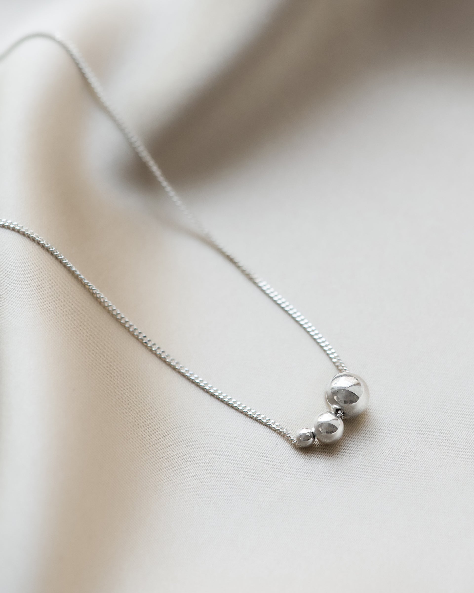 A product shot of the Universe Necklace Silver, featuring a fine chain adorned with three polished silver balls in varying sizes.