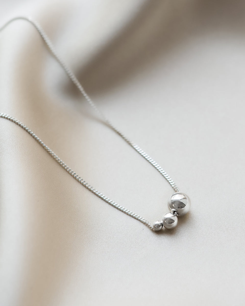 A product shot of the Universe Necklace Silver, featuring a fine chain adorned with three polished silver balls in varying sizes.