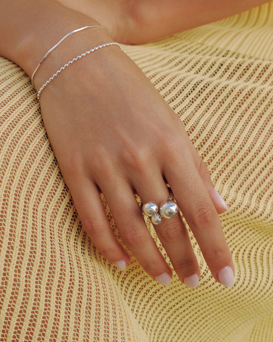 A close-up shot of a model's hand wearing the Universe Ring in silver, featuring three polished spheres. She also wears two matching silver bracelets: the fine Sheer Mirror Bracelet and the beaded Lunetta Bracelet.