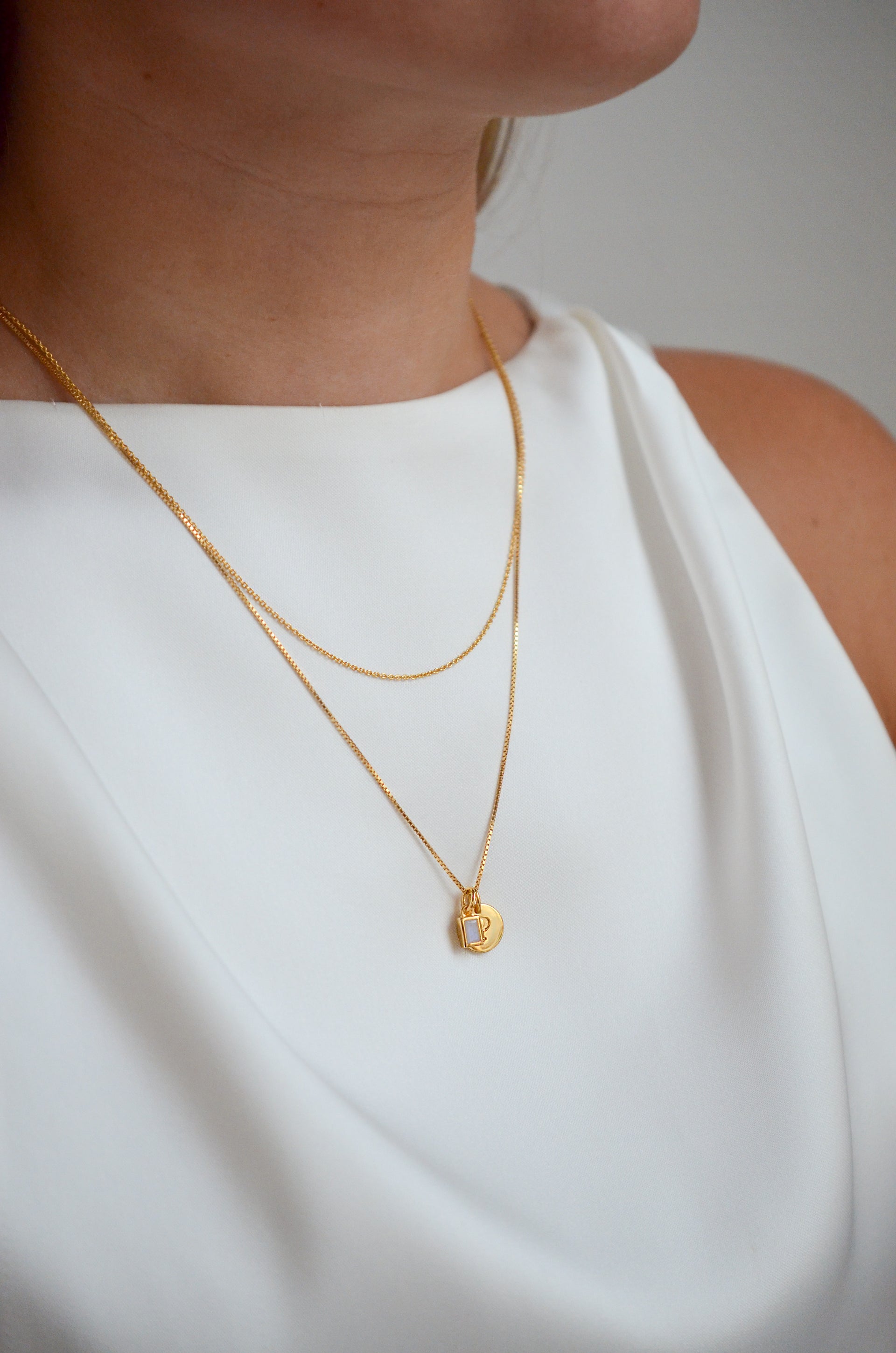 One short gold chain and one medium long gold chain with a gold mini letter and a gold pendant with white onyx